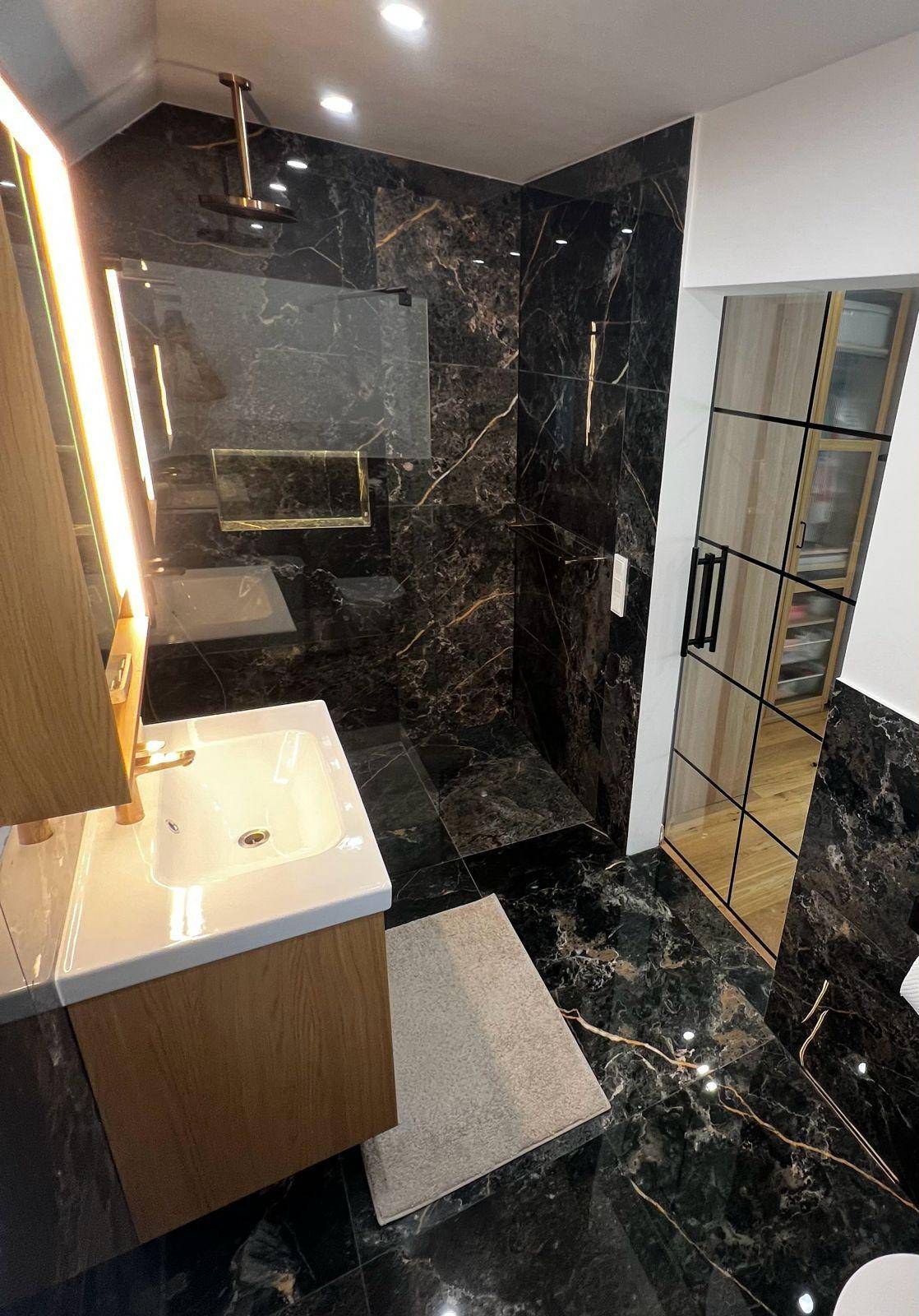 Modernes Badezimmer mit dunklen Marmorfliesen, begehbarer Dusche und elegantem Holzwaschtisch.