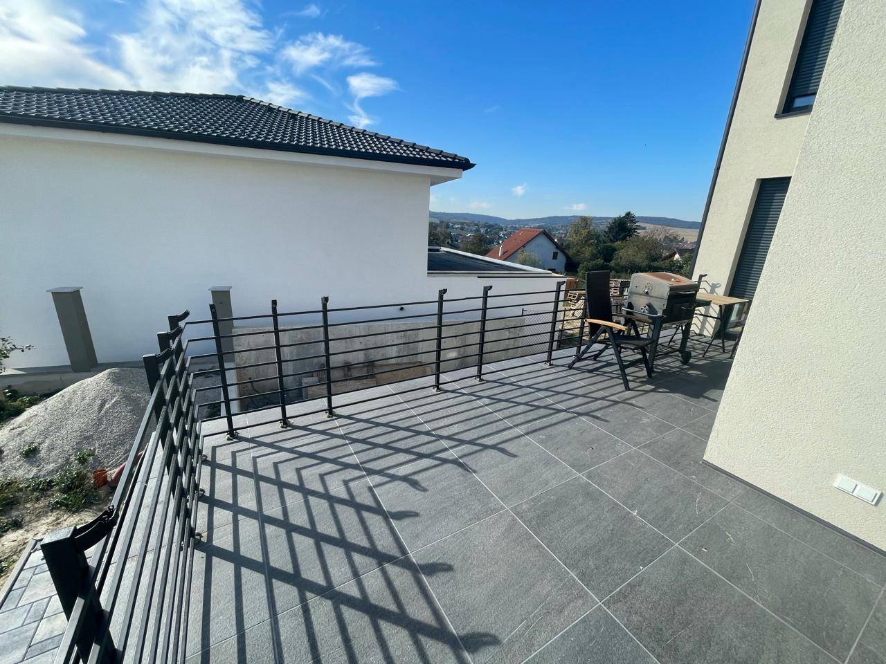 Geräumige obere Terrasse mit Fliesenboden, Metallgeländer und Sitzgelegenheiten im Freien.