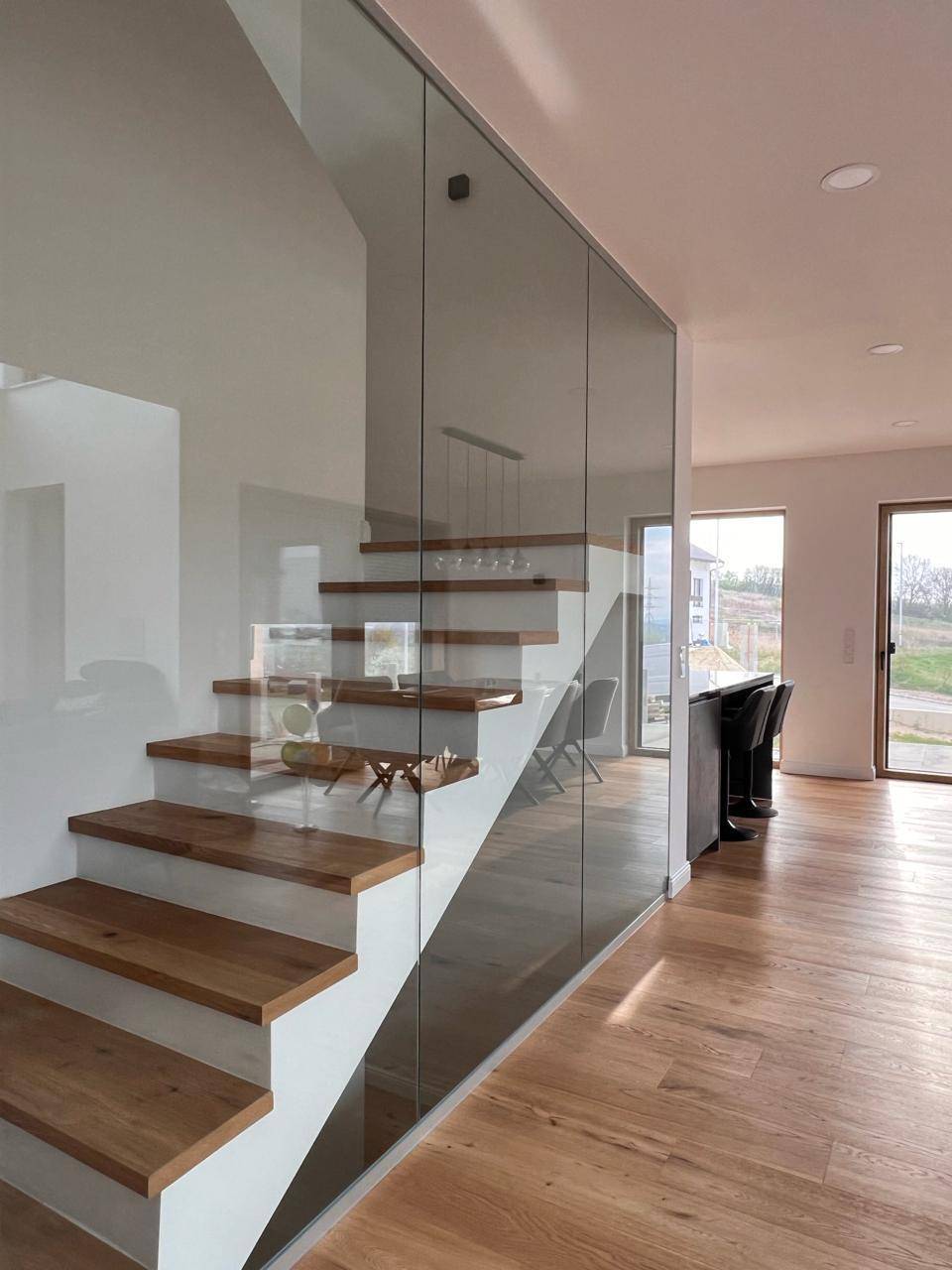 Moderne Holztreppe mit Glasgeländer, die den offenen Wohnbereich elegant verbindet.