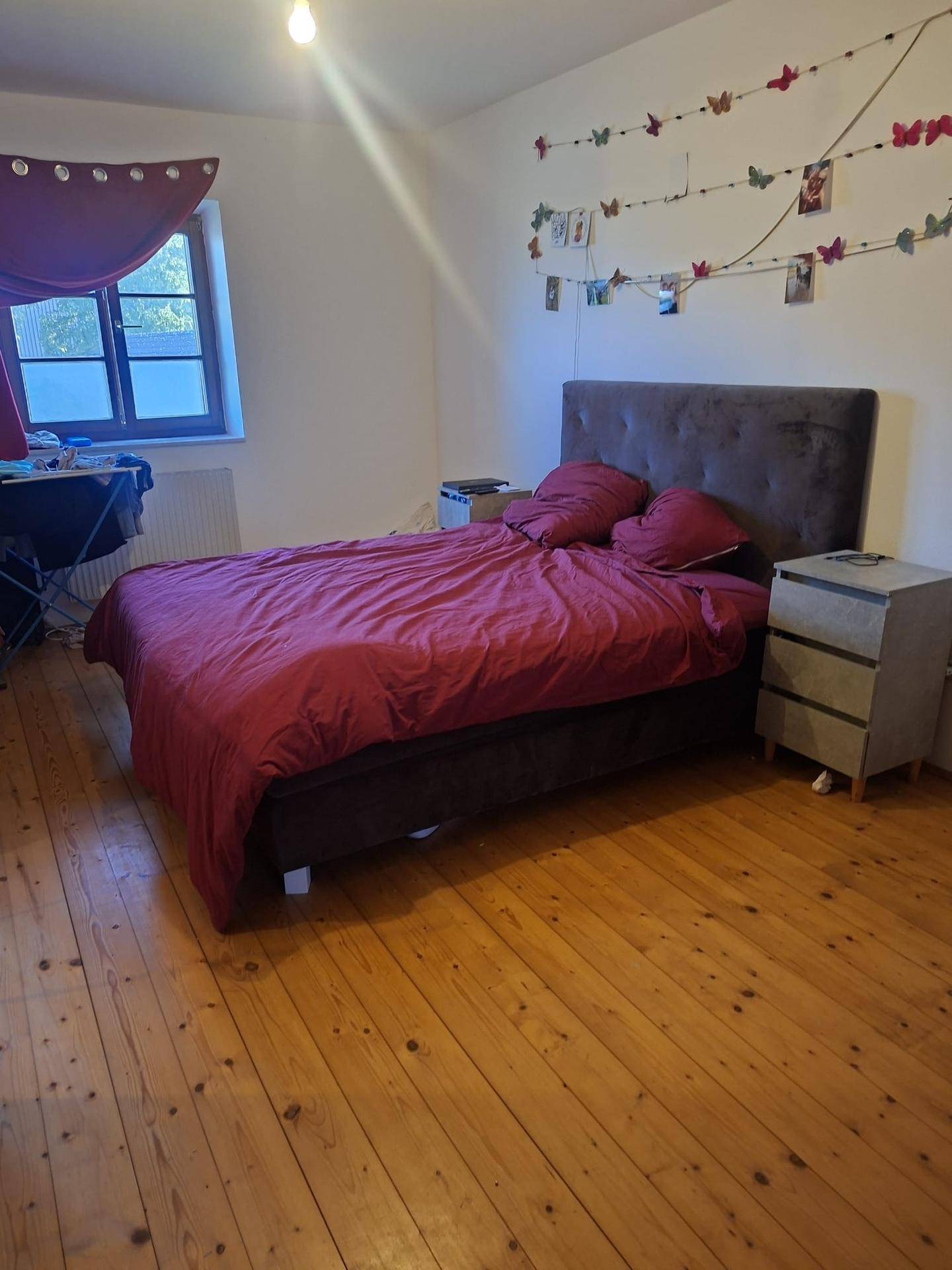 Schlafzimmer mit Doppelbett, Holzboden und Fenster, dekoriert mit persönlichen Akzenten.