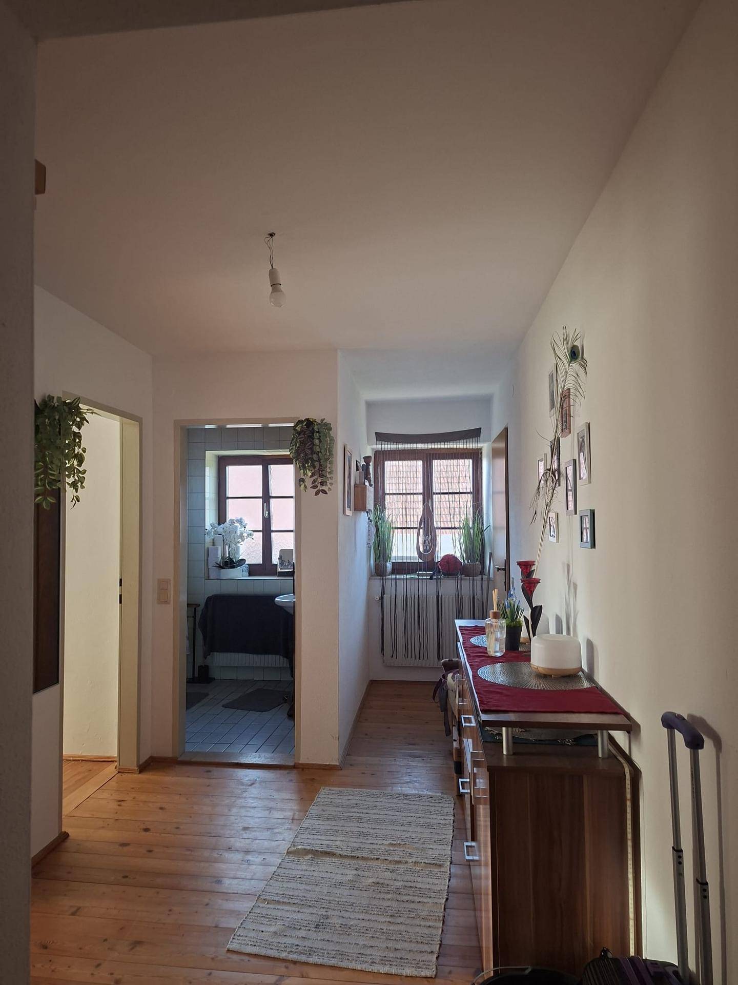 Heller Flur mit Holzfußboden und dekorativer Kommode, der zu weiteren Räumen führt.