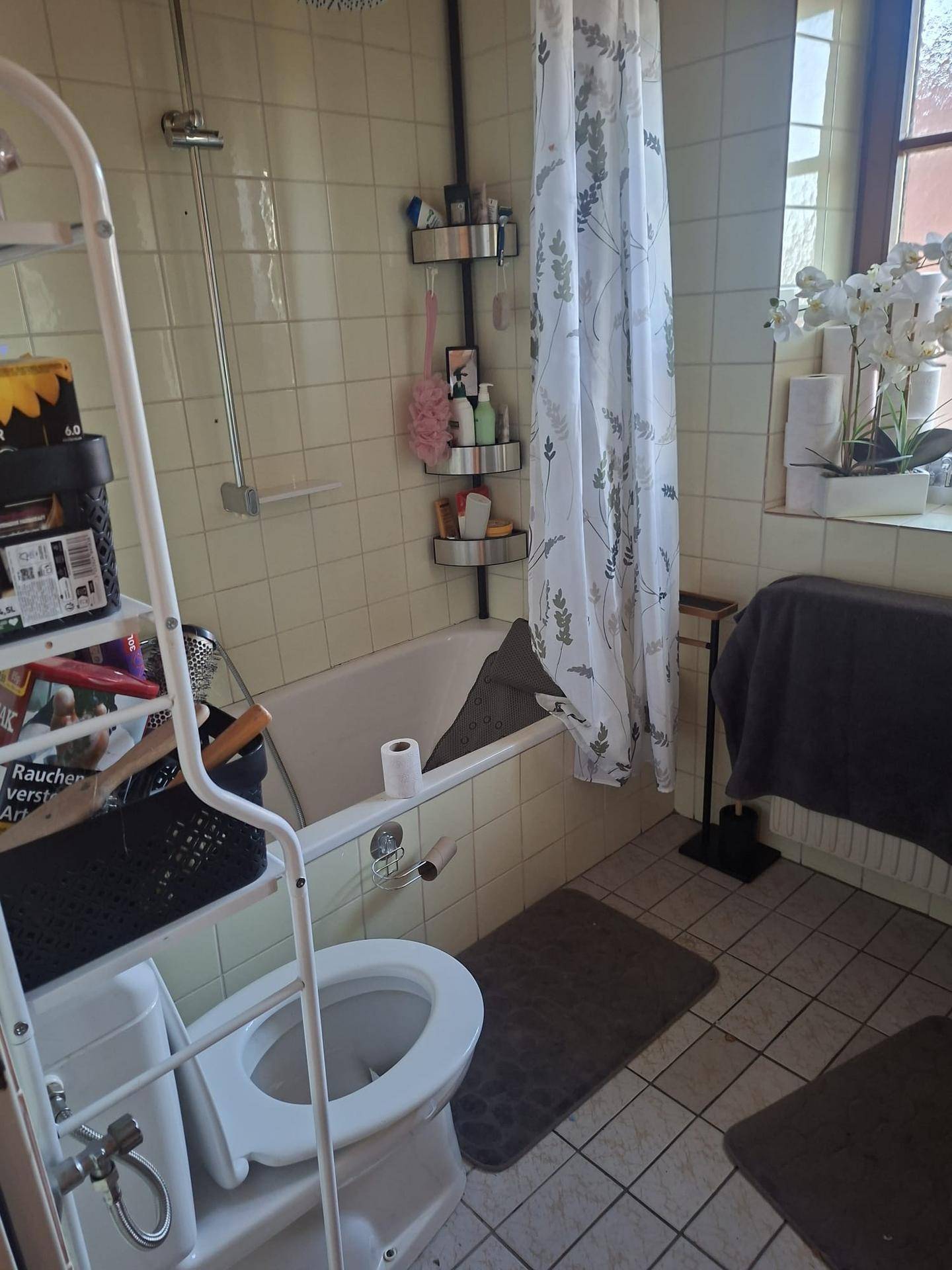 Badezimmer mit Badewanne, Toilette und Fenster, ausgestattet mit hellen Fliesen und Duschvorhang.
