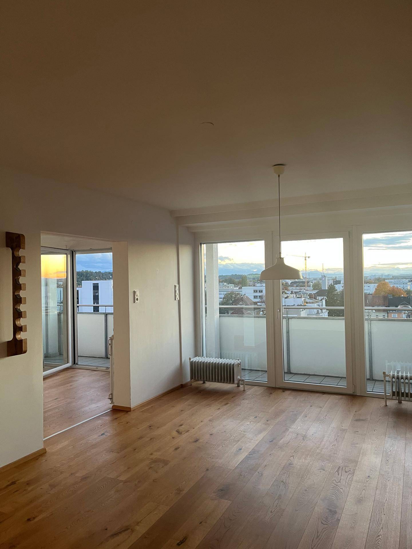 Heller Wohnraum mit Holzboden, großen Fenstern und direktem Zugang zu einem Balkon.
