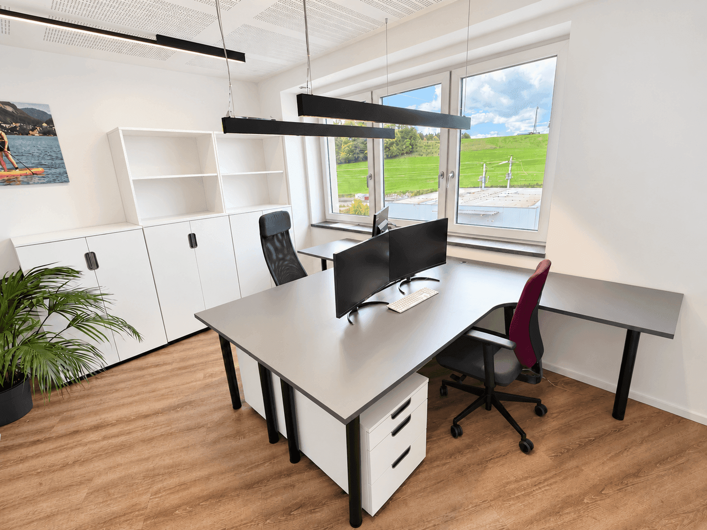 Helles Büro mit zwei Arbeitsplätzen, Schränken und Blick auf eine grüne Landschaft.
