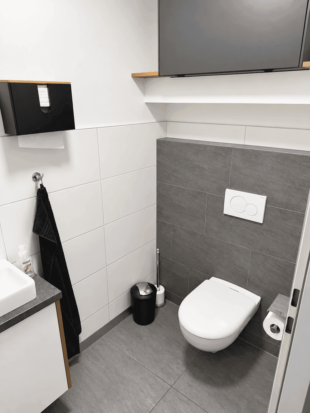 Modernes Gäste-WC mit grauen und weißen Fliesen, wandhängendem WC und kleinem Waschbecken.