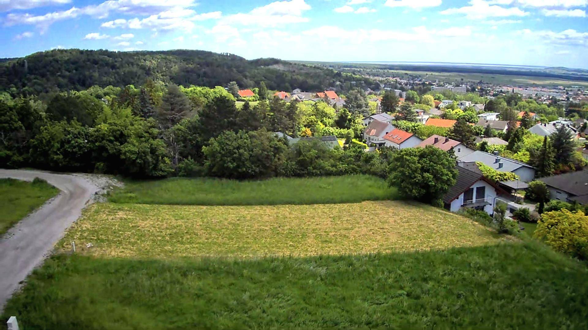 Weitläufiger Blick über eine Wohnsiedlung, grüne Hügel und einen See in der Ferne.