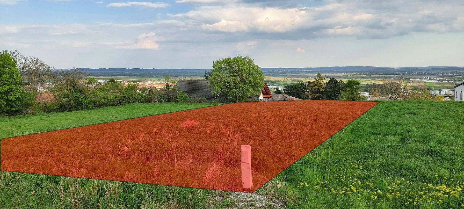 Grünfläche mit markiertem Grundstück und weitem Blick über die Landschaft unter bewölktem Himmel.