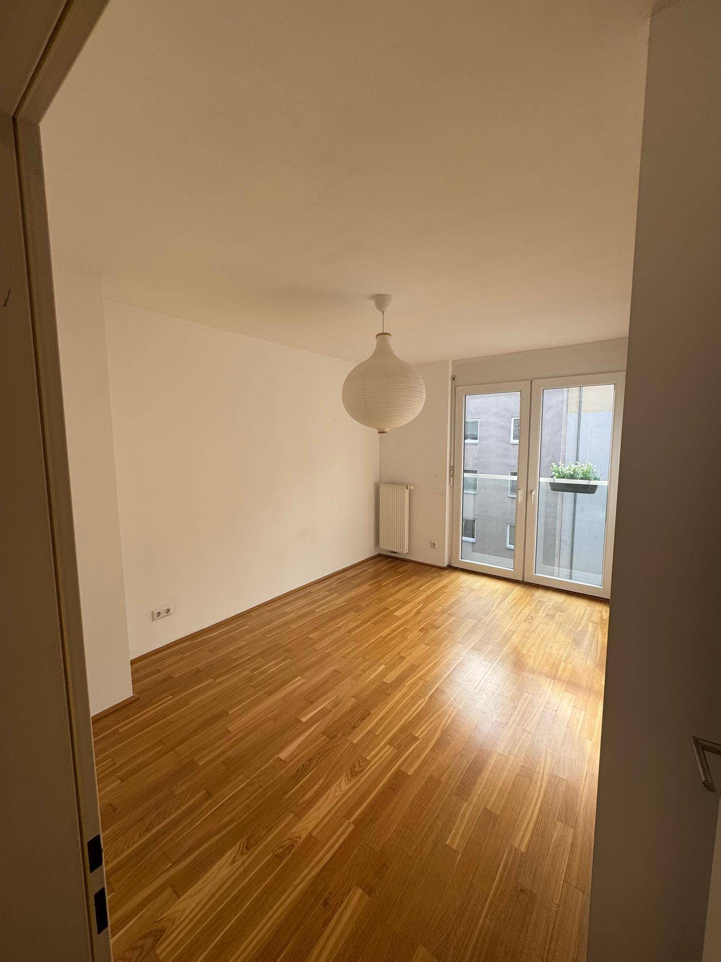 Geräumiges, leeres Zimmer mit Parkettboden und direktem Zugang zu einem französischen Balkon.