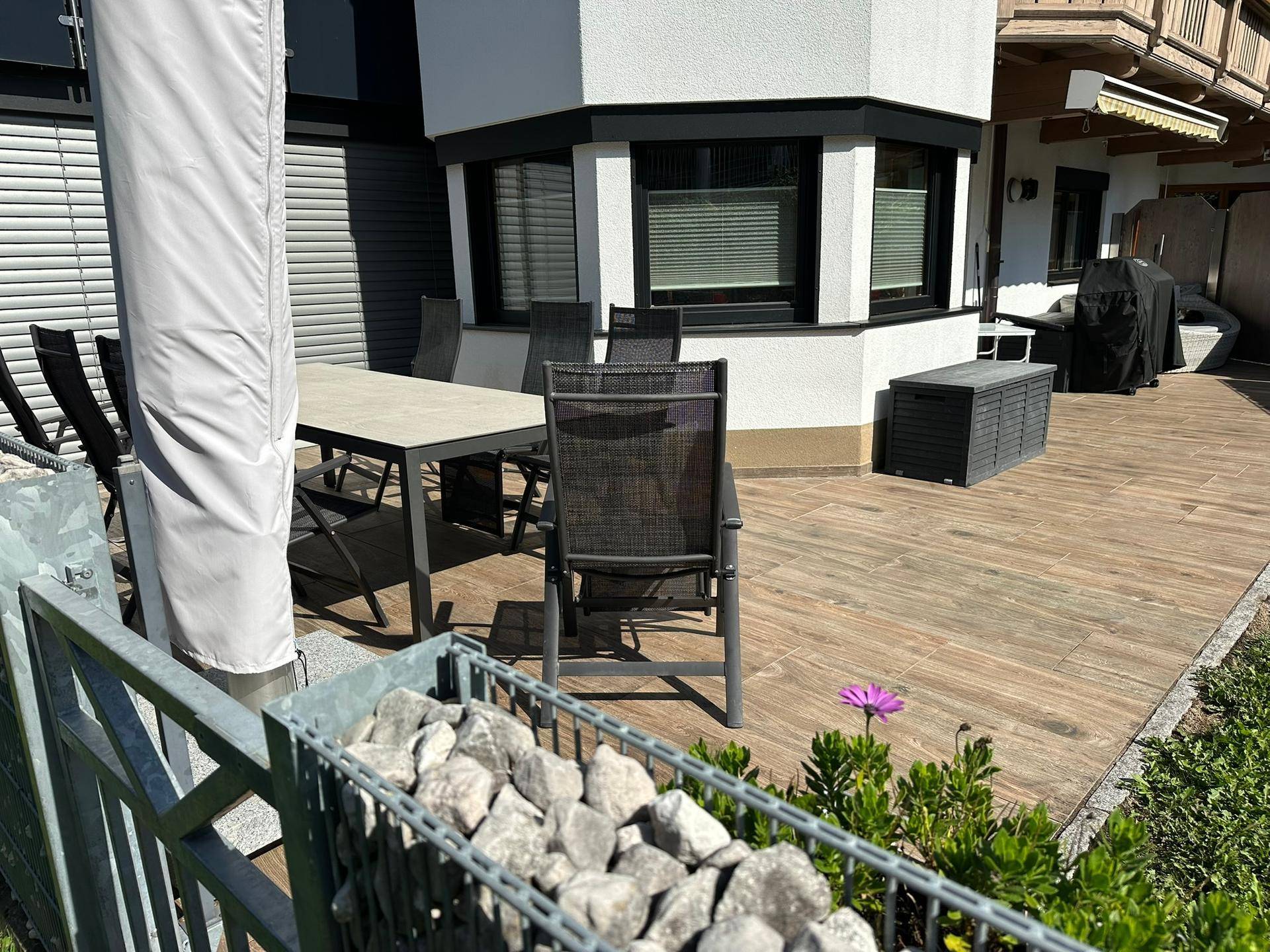 Geräumige Terrasse mit Outdoor-Möbeln und Gabionenwand, ideal für Entspannung im Freien.