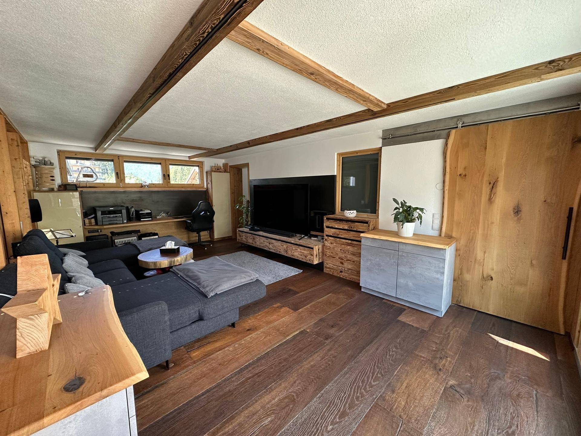 Geräumiges Wohnzimmer mit sichtbaren Holzbalken, dunklem Holzboden und moderner Einrichtung.