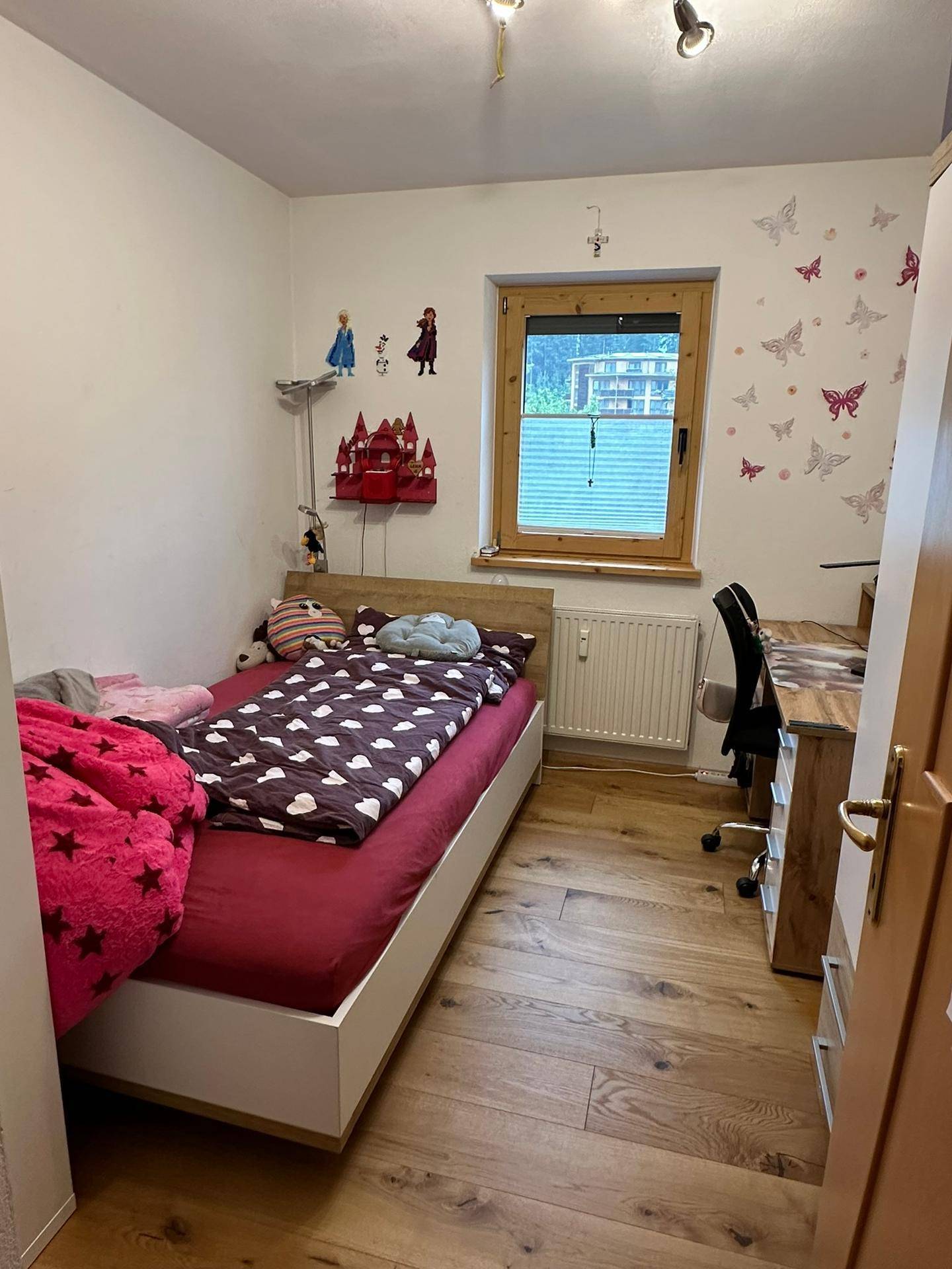 Helles Kinderzimmer mit Einzelbett, Schreibtisch und Fenster mit Blick ins Grüne.