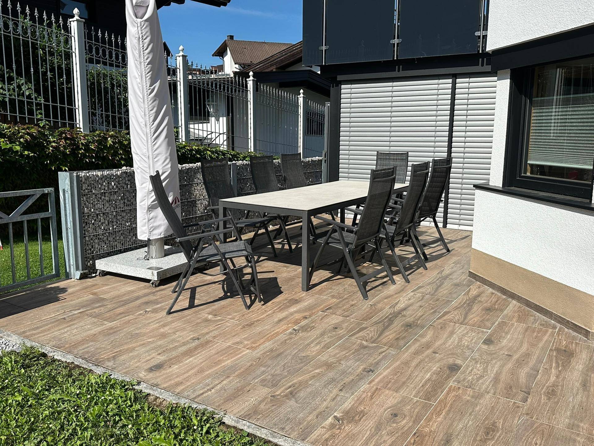 Sonnige Terrasse mit großem Esstisch und Stühlen, umgeben von Grünflächen und Privatsphäre.