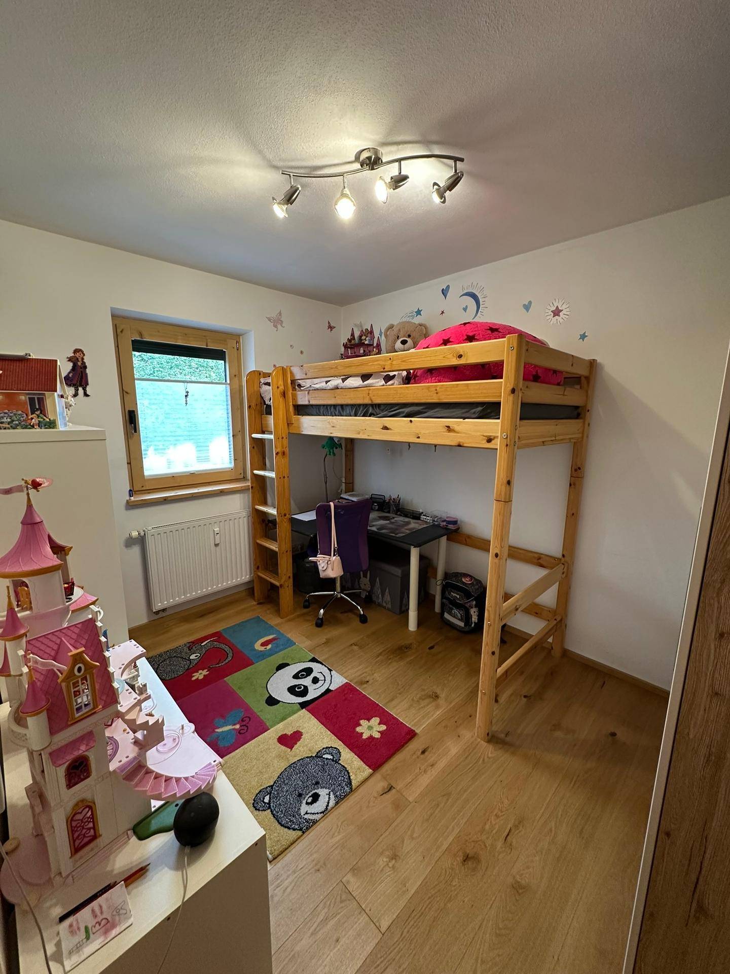 Kinderzimmer mit Hochbett, Schreibtisch und farbenfrohem Teppich für eine spielerische Einrichtung.
