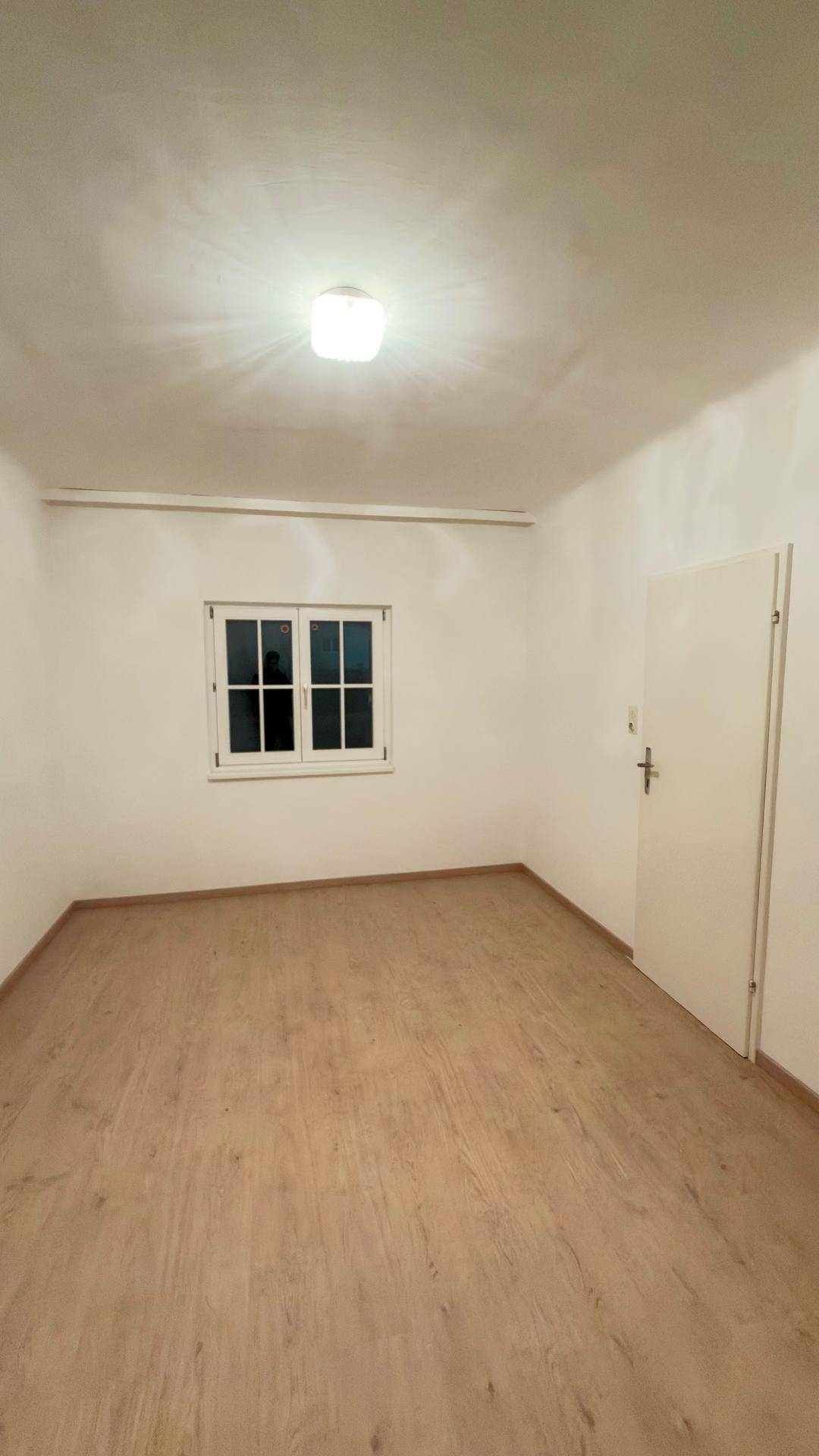 Helles Schlafzimmer mit Laminatboden und einem Fenster, das viel Tageslicht hereinlässt.