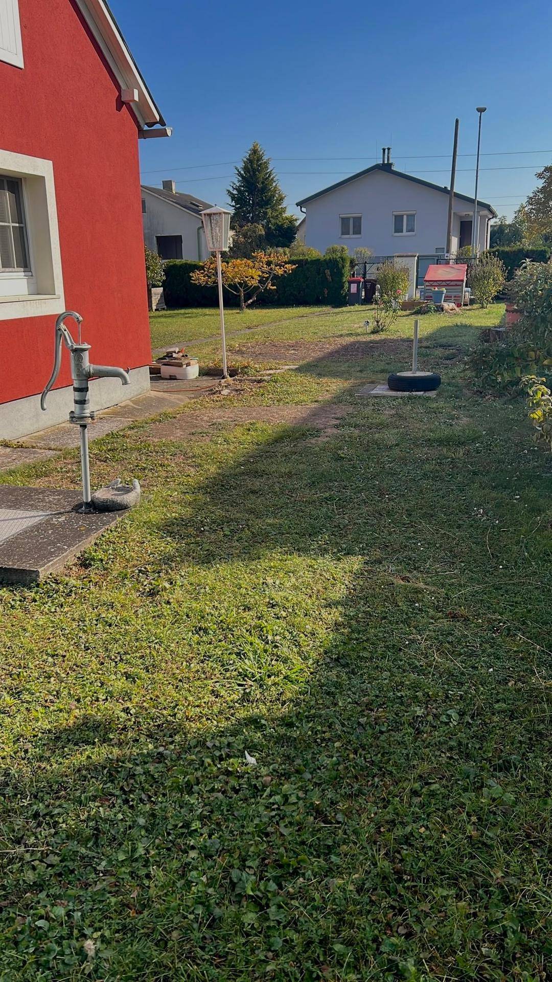 Seitlicher Blick auf den Gartenbereich des Hauses mit einer alten Wasserpumpe und Rasenfläche.