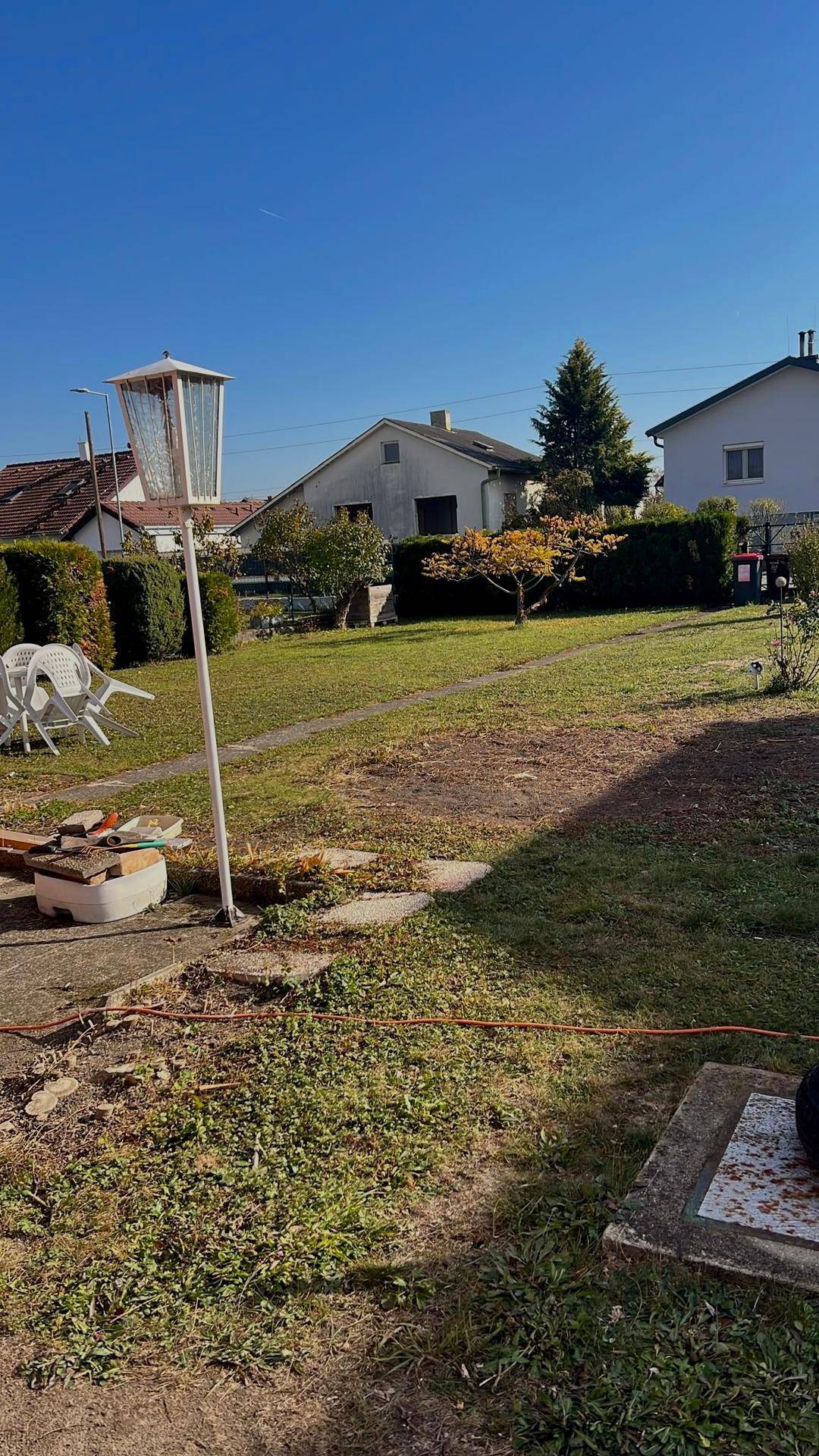 Weitläufiger Gartenbereich mit Rasen, Gartenlaterne und Blick auf die Nachbarschaft.