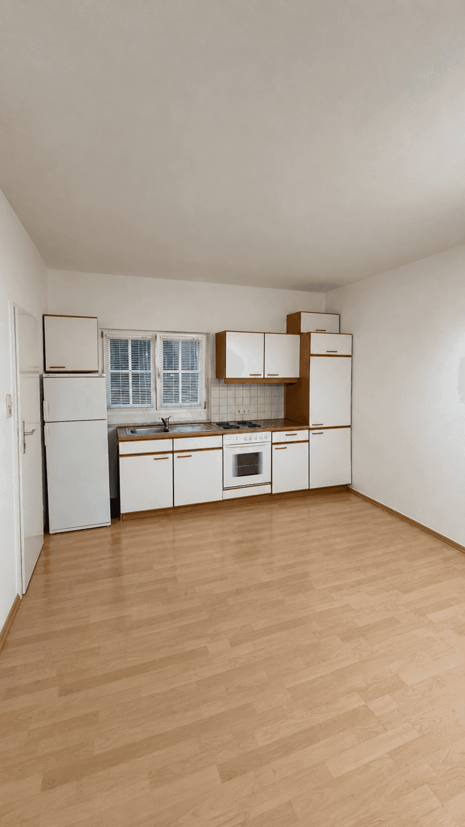 Funktionale Küche mit weißen Schränken, Holztheke und grundlegenden Elektrogeräten.