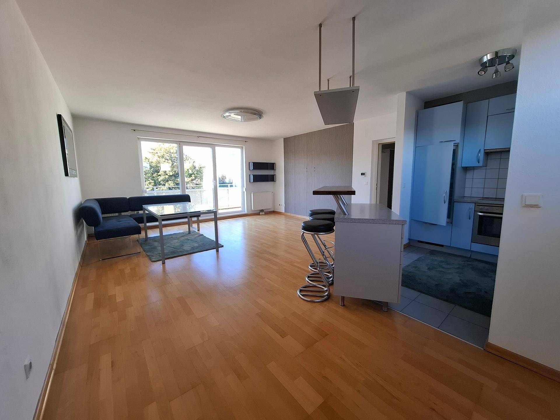 Geräumiger offener Wohnbereich mit Holzboden, Sofa und integrierter Küchenzeile mit Frühstücksbar.