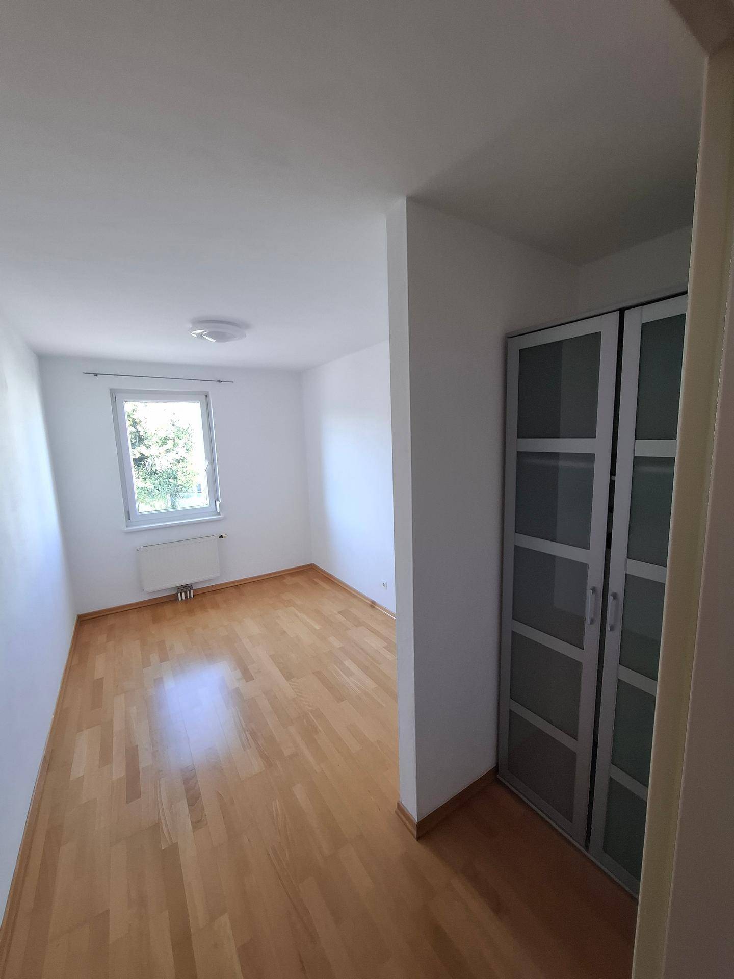 Helles Schlafzimmer mit Holzboden, weiß gestrichenen Wänden und einem praktischen Einbauschrank.