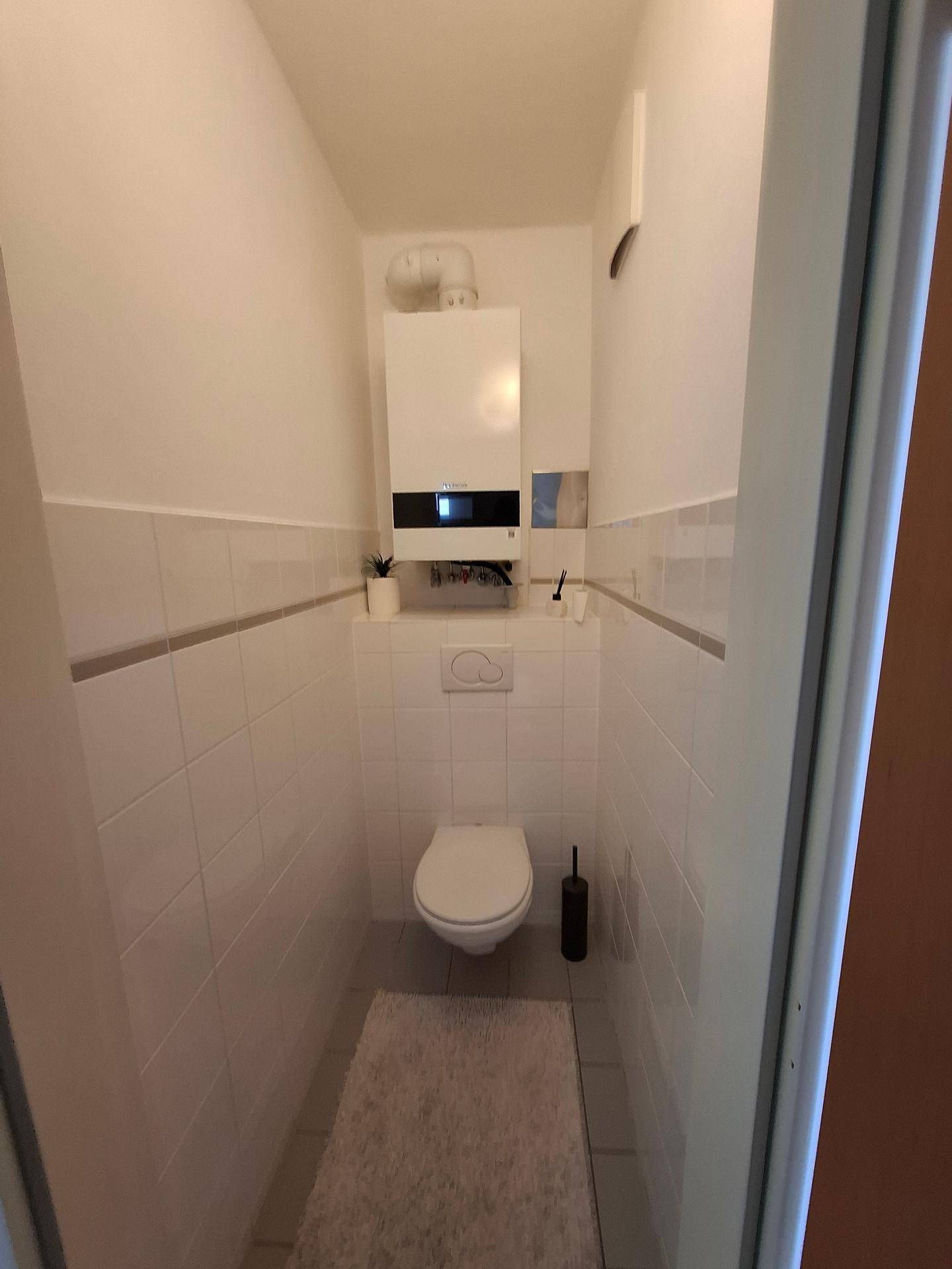 Kleines WC mit wandhängender Toilette und einem Heizkessel, funktional und sauber.