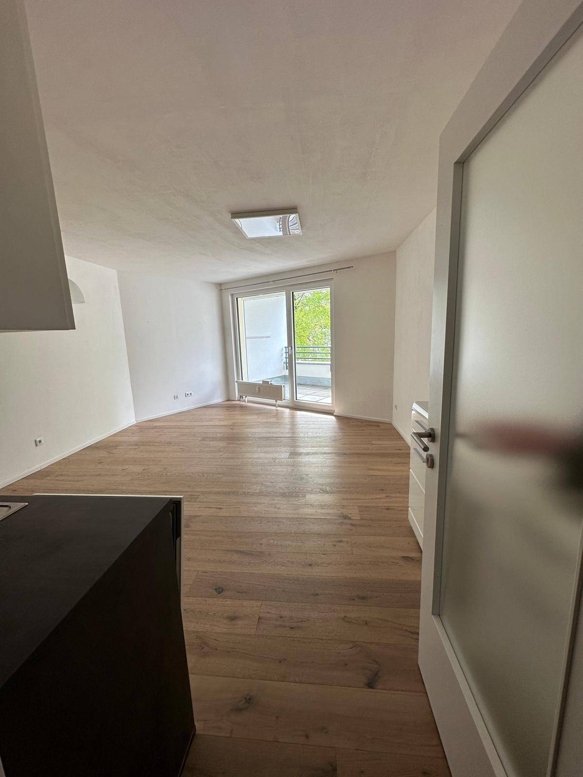 Geräumiges Wohnzimmer mit Holzboden und Zugang zu einem sonnigen Balkon durch eine große Glastür.