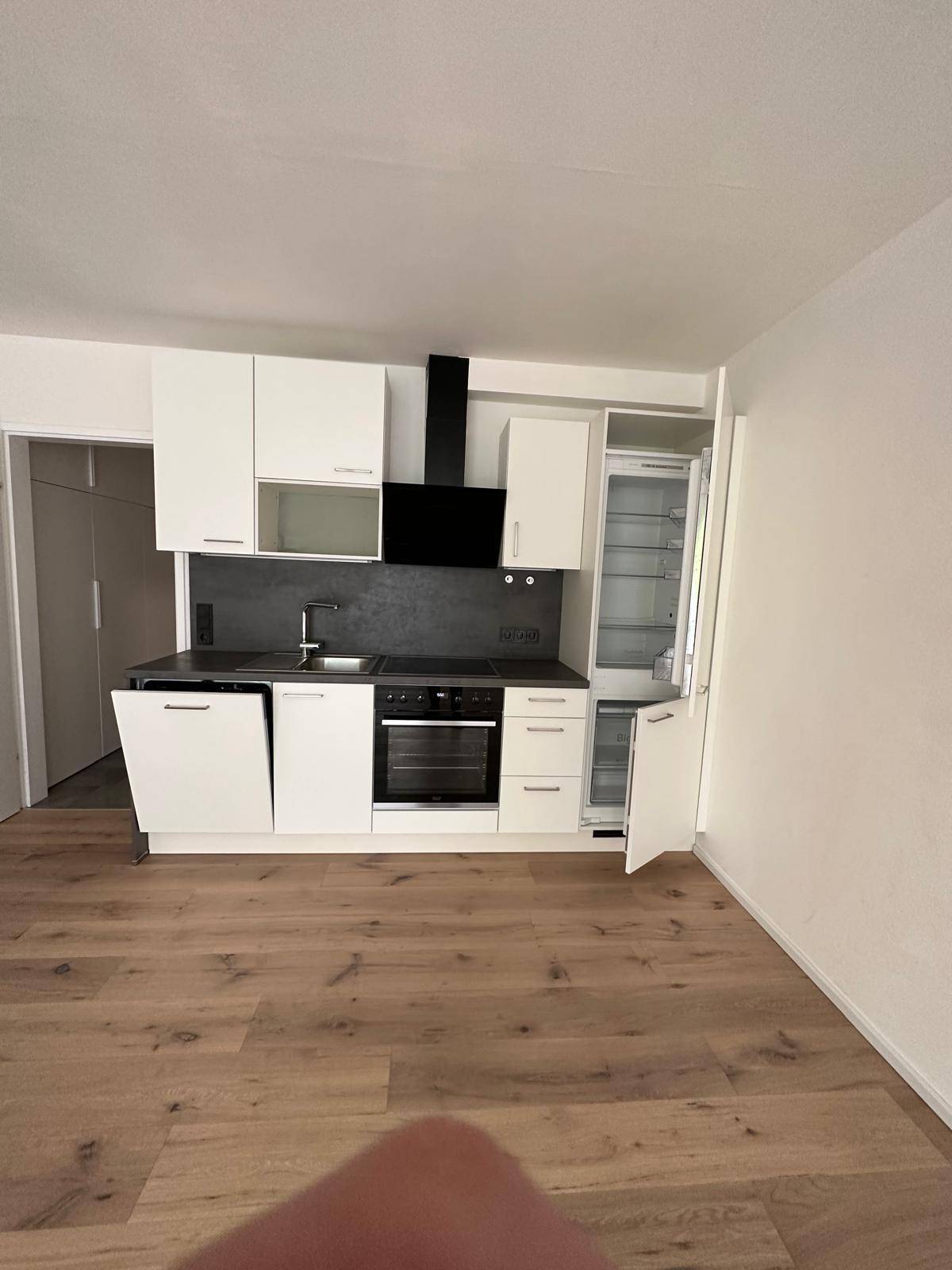 Moderne Einbauküche mit weißen Schränken, schwarzer Arbeitsplatte und integrierten Elektrogeräten.