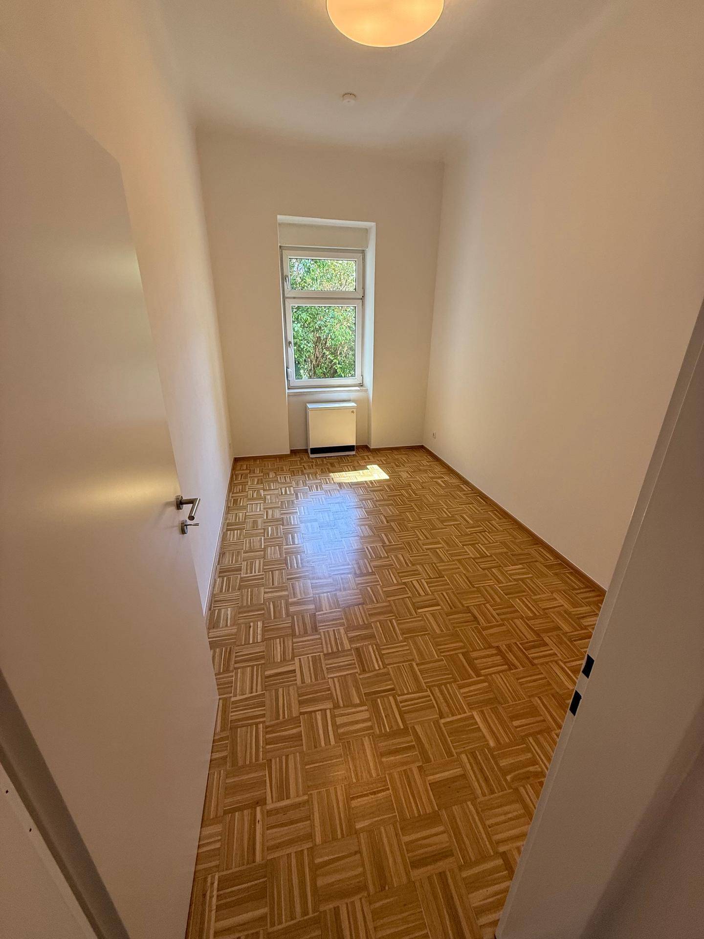 Leeres Schlafzimmer mit hellem Parkettboden und einem Fenster für natürliche Belichtung.