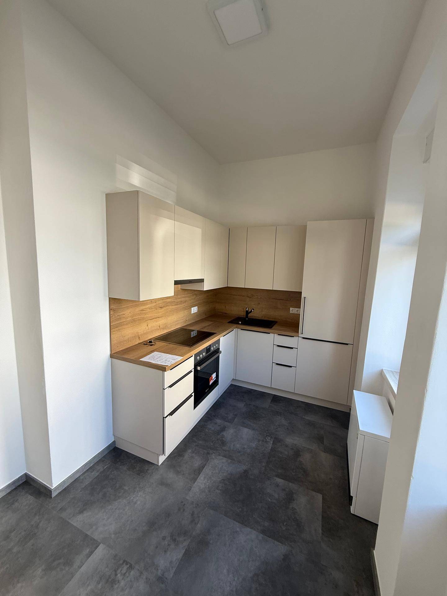Moderne Einbauküche mit hellen Schränken, Holzoptik-Arbeitsplatte und dunklem Fliesenboden.