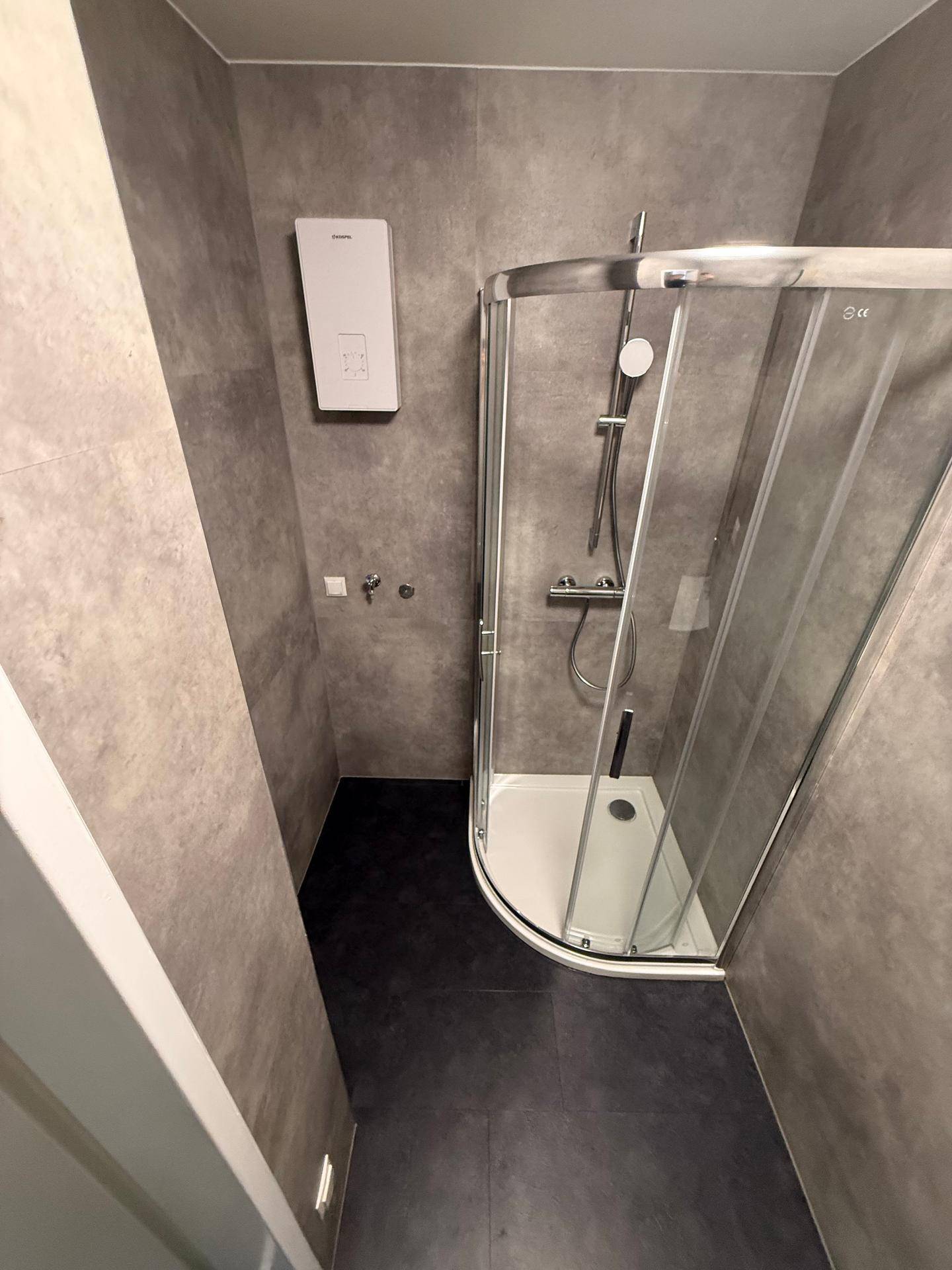 Modernes Badezimmer mit grauen Fliesen und einer Eckdusche mit Glasabtrennung.