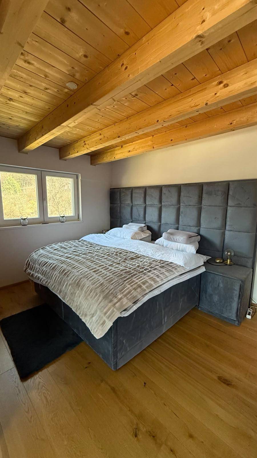 Gemütliches Schlafzimmer mit großem Bett, Holzboden und sichtbaren Deckenbalken sowie Fensterblick.