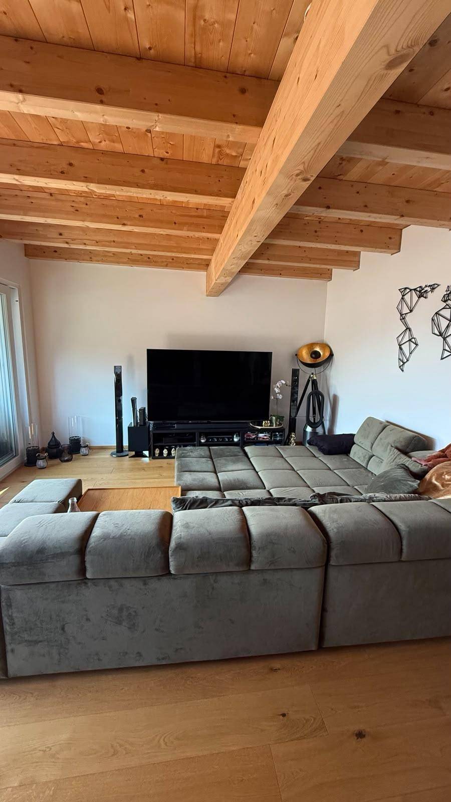 Geräumiges Wohnzimmer mit großem Ecksofa, Fernseher, Holzboden und sichtbaren Deckenbalken.