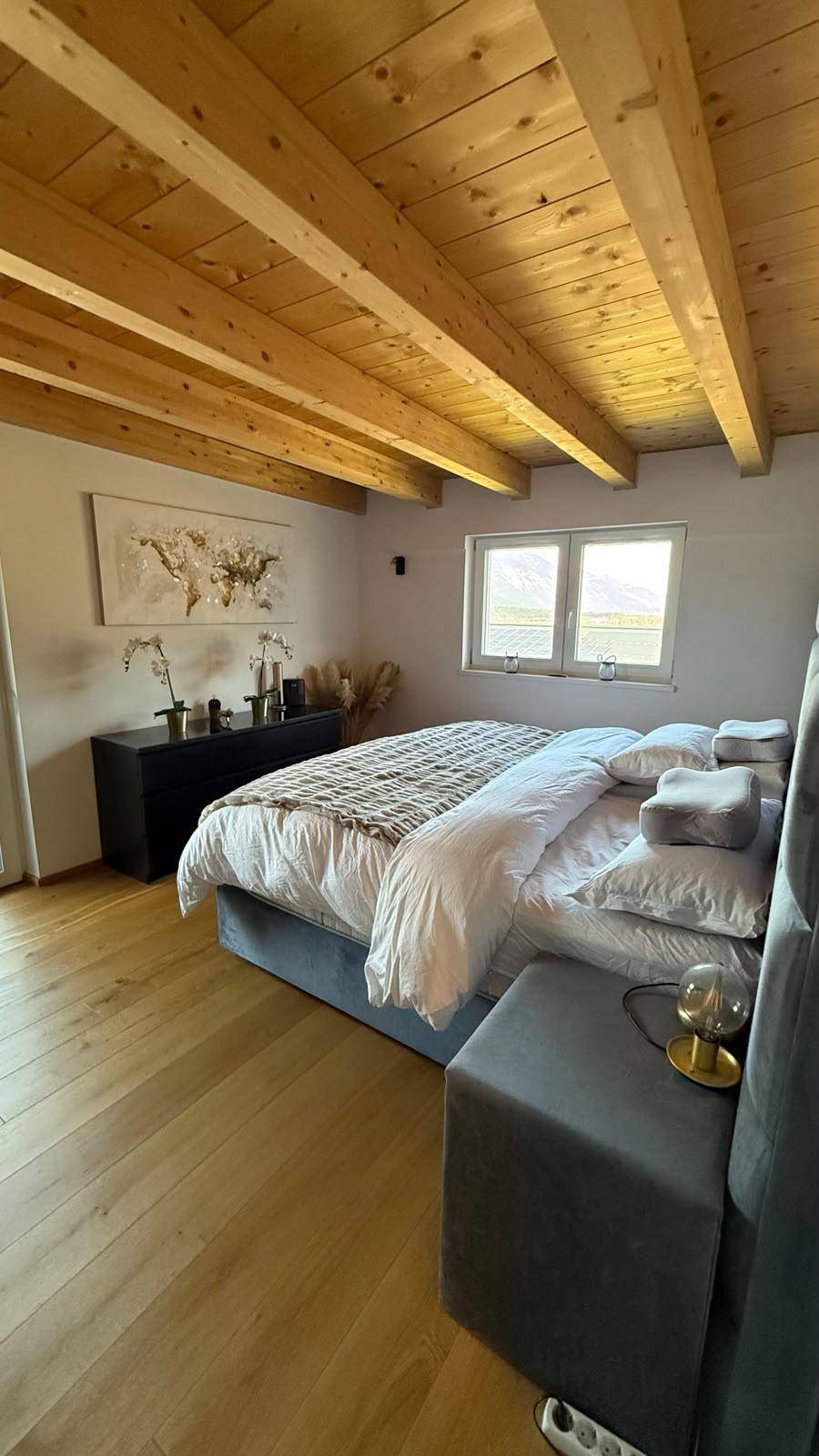 Helles Schlafzimmer mit großem Bett, Holzboden, Holzbalkendecke und Blick nach draußen.