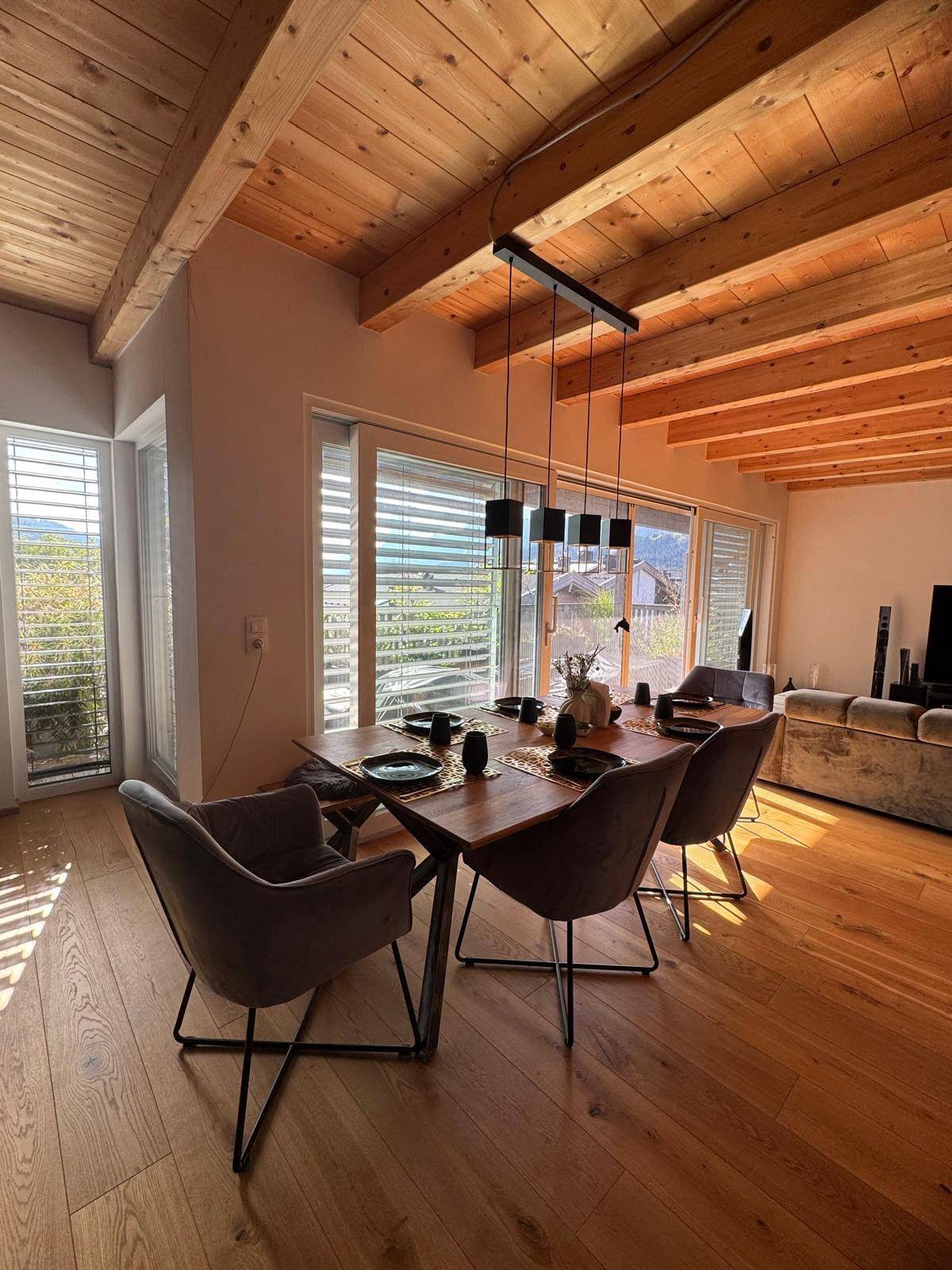 Heller Essbereich mit Holztisch, modernen Stühlen, großen Fenstern und Holzbalkendecke.