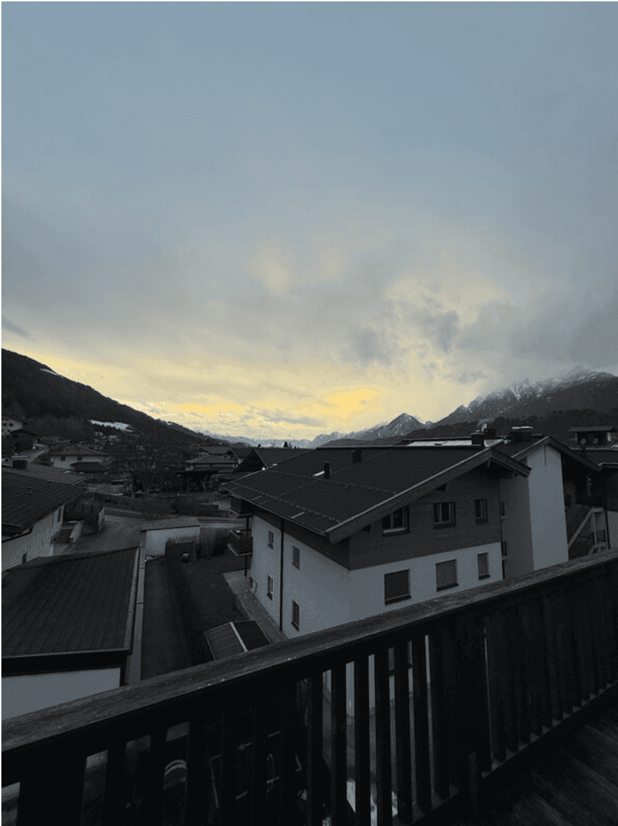 Panoramablick von einem Balkon über eine Stadt auf die umliegenden Berge bei Sonnenuntergang.