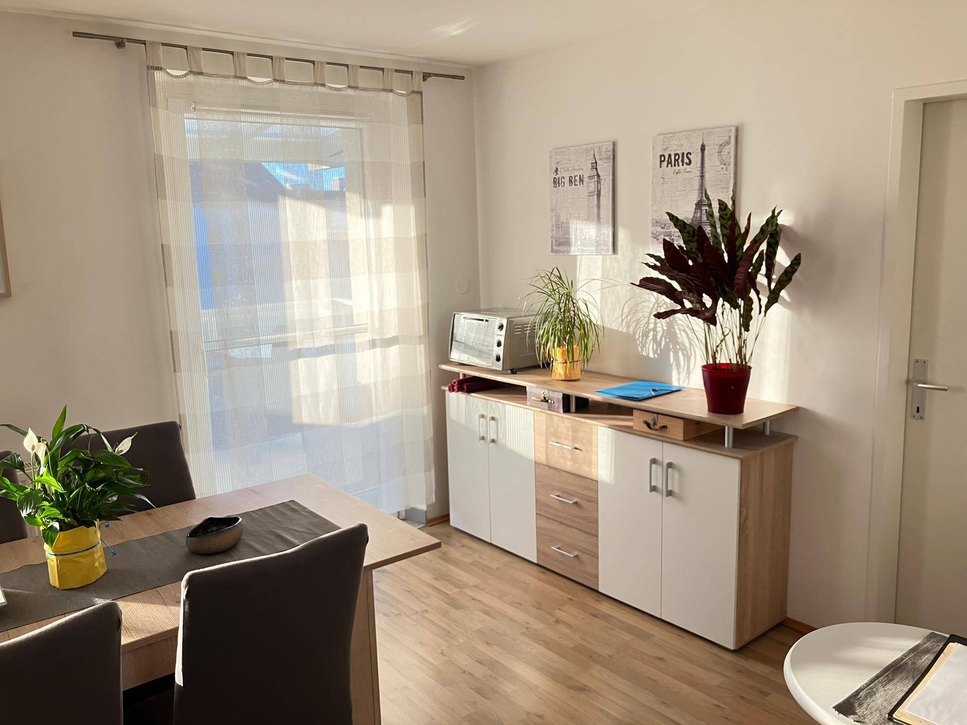 Heller Essbereich mit Holztisch, Sideboard und großem Fenster, das viel Tageslicht hereinlässt.