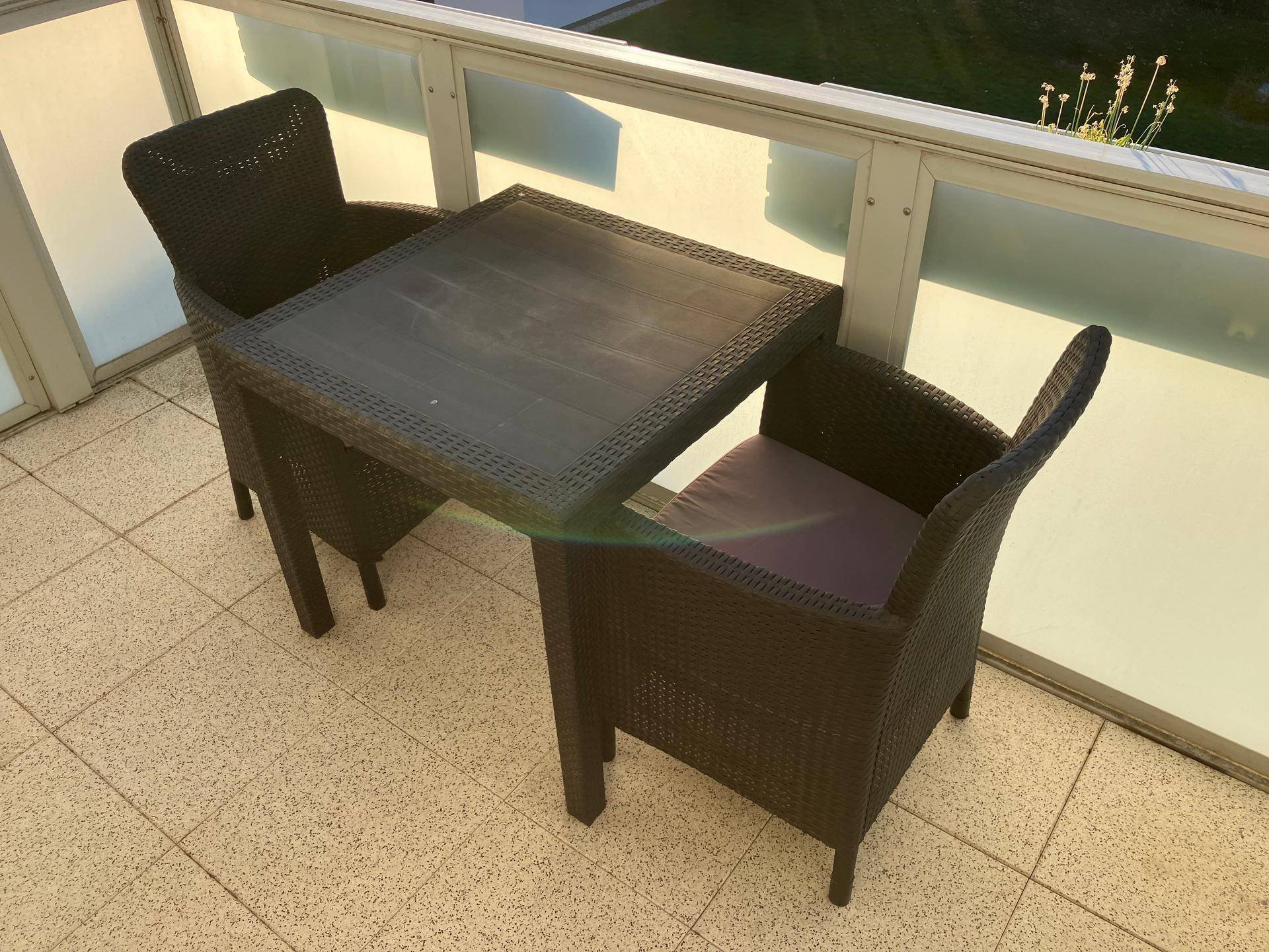 Kleiner Balkon mit Rattan-Sitzgruppe und Fliesenboden, ideal für entspannte Stunden im Freien.