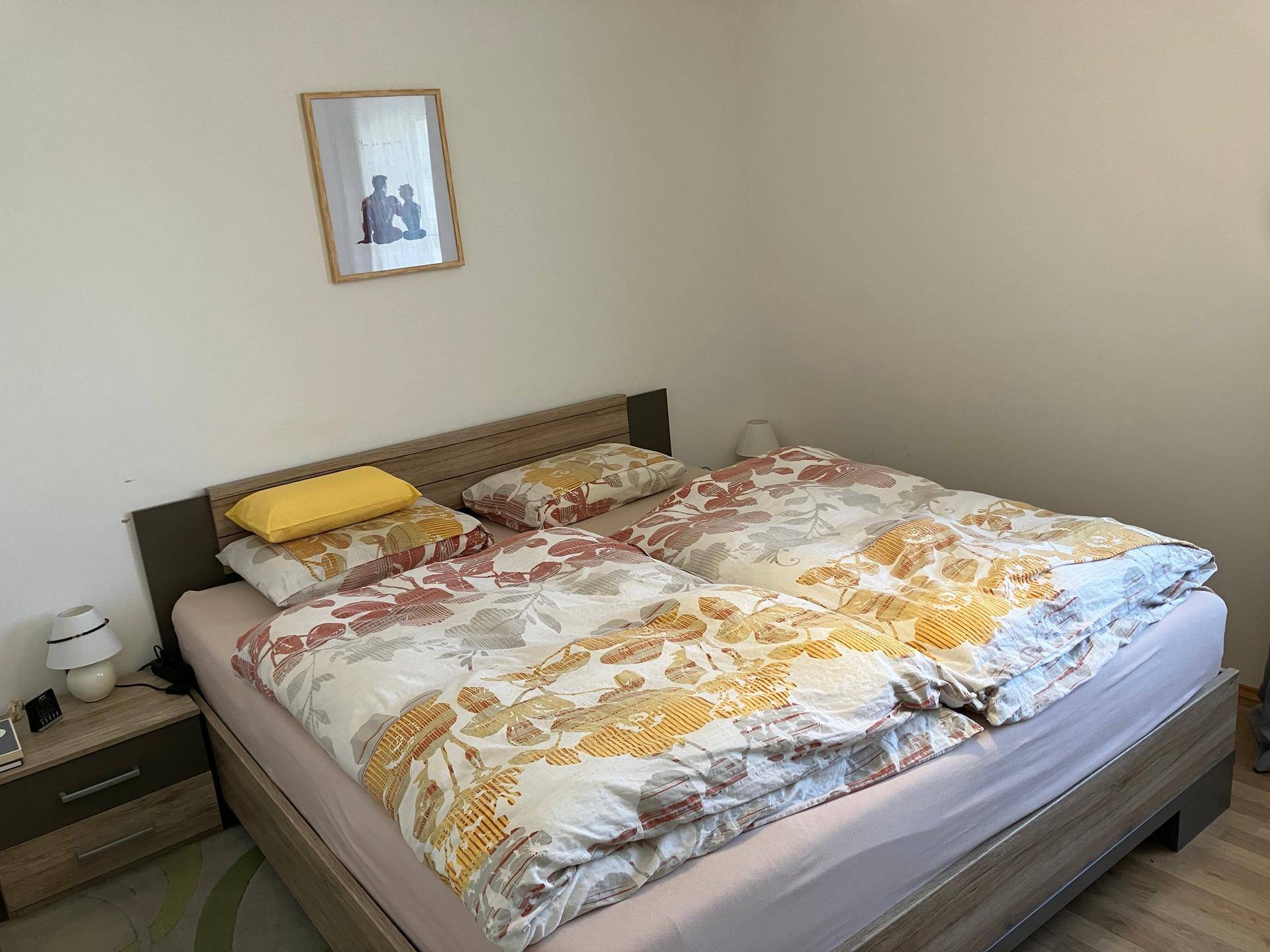 Schlafzimmer mit Doppelbett, Nachttischen und floral gemusterter Bettwäsche in warmen Tönen.