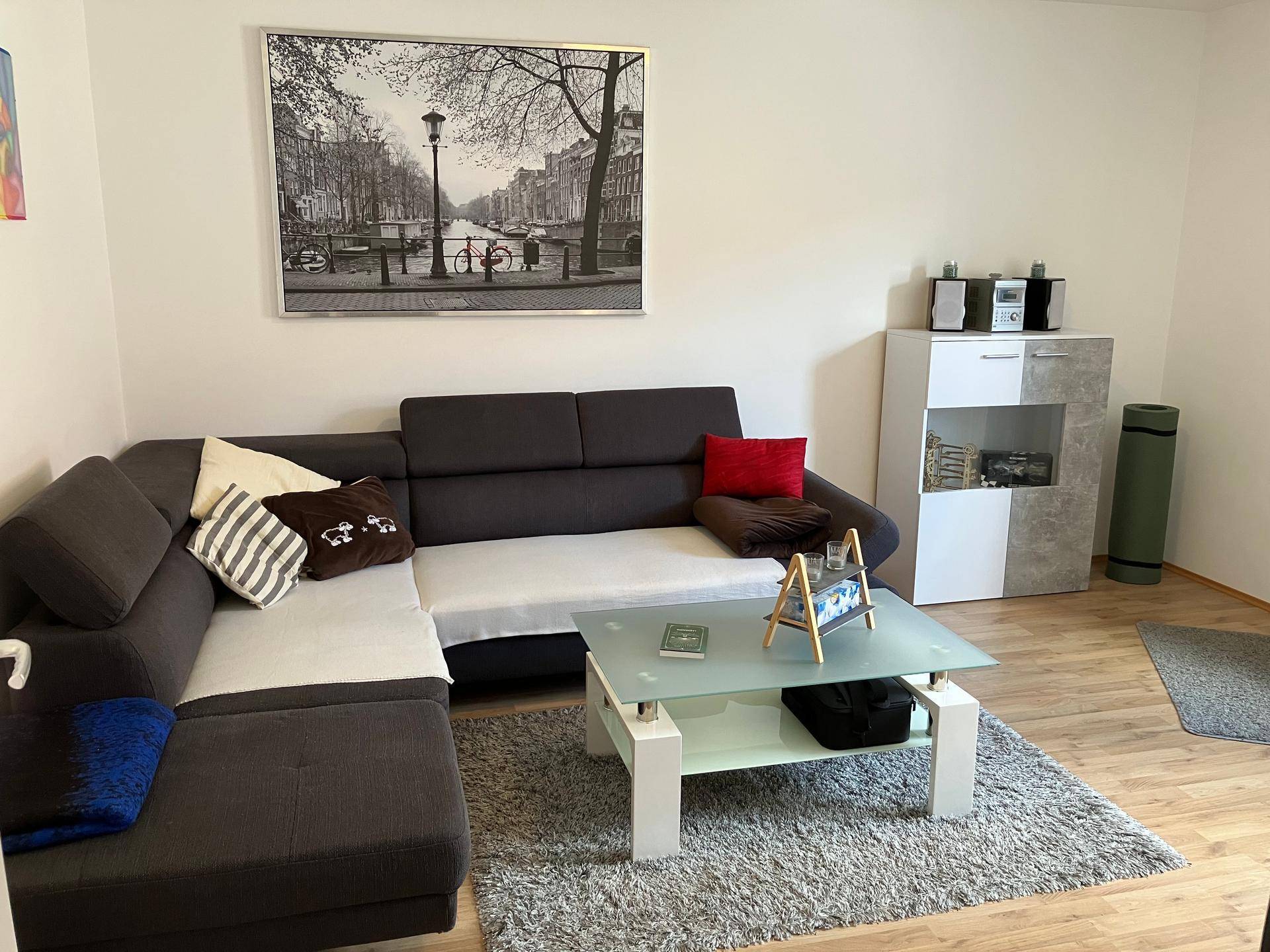 Gemütliches Wohnzimmer mit Ecksofa, Couchtisch und einem großen Schwarz-Weiß-Bild an der Wand.