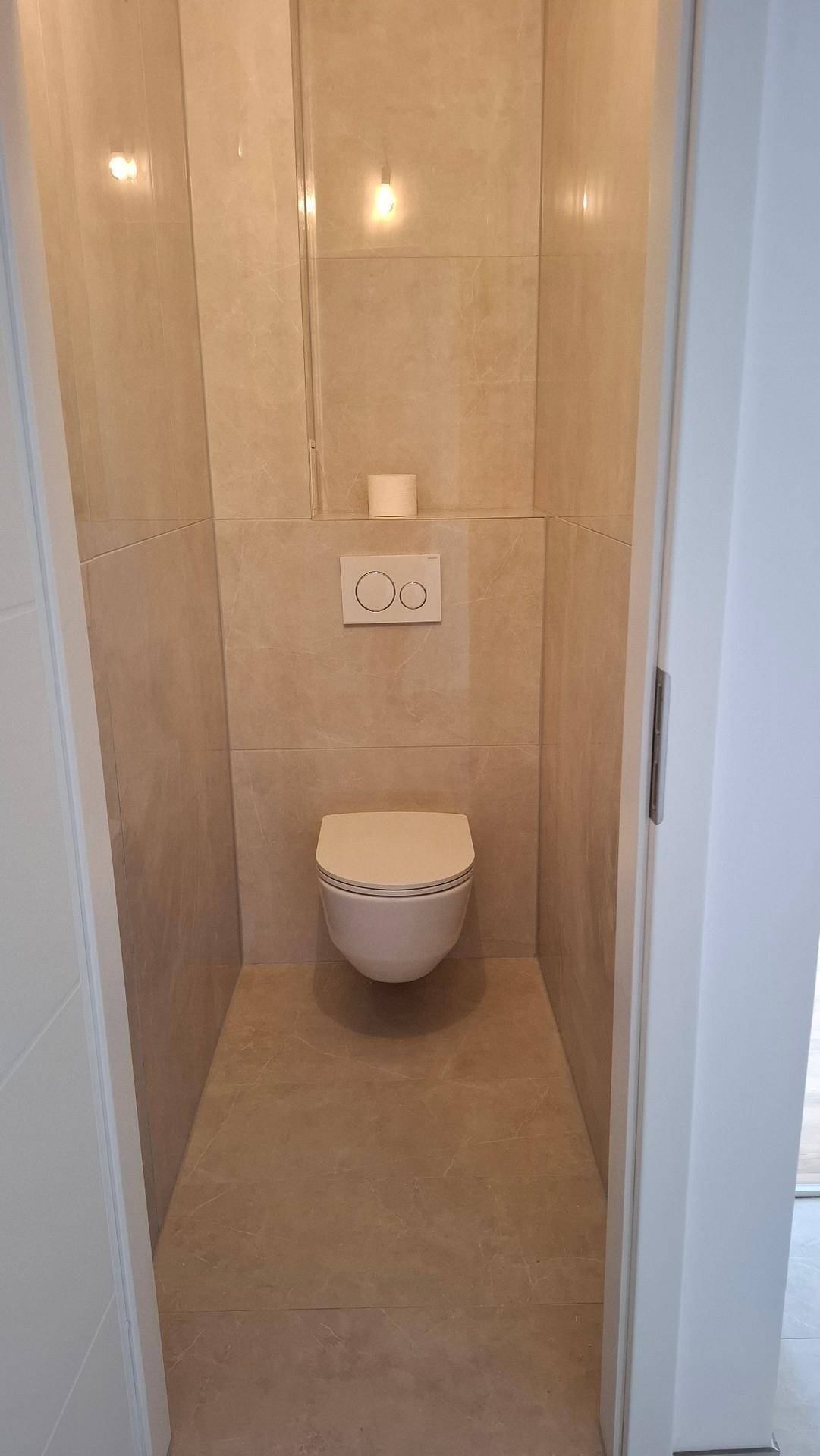 Separates WC mit wandhängender Toilette und modernen Fliesen an Wänden und Boden.