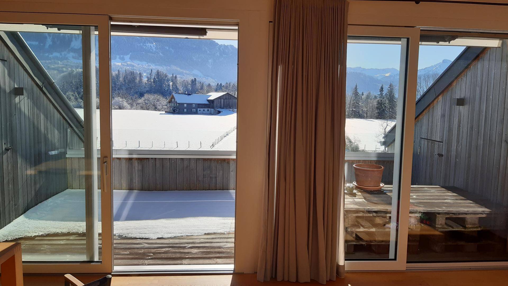 Winterlicher Ausblick vom Balkon auf verschneite Felder und die umliegende Berglandschaft.