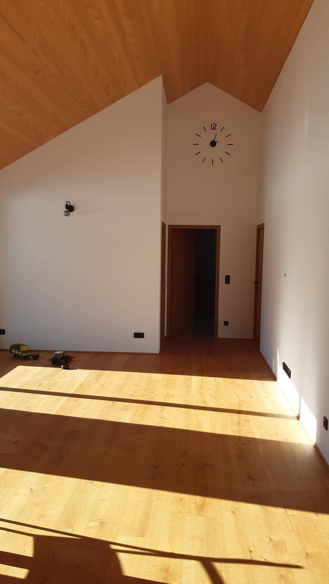 Heller Flurbereich mit Holzboden, schräger Decke und einer minimalistischen Wanduhr.