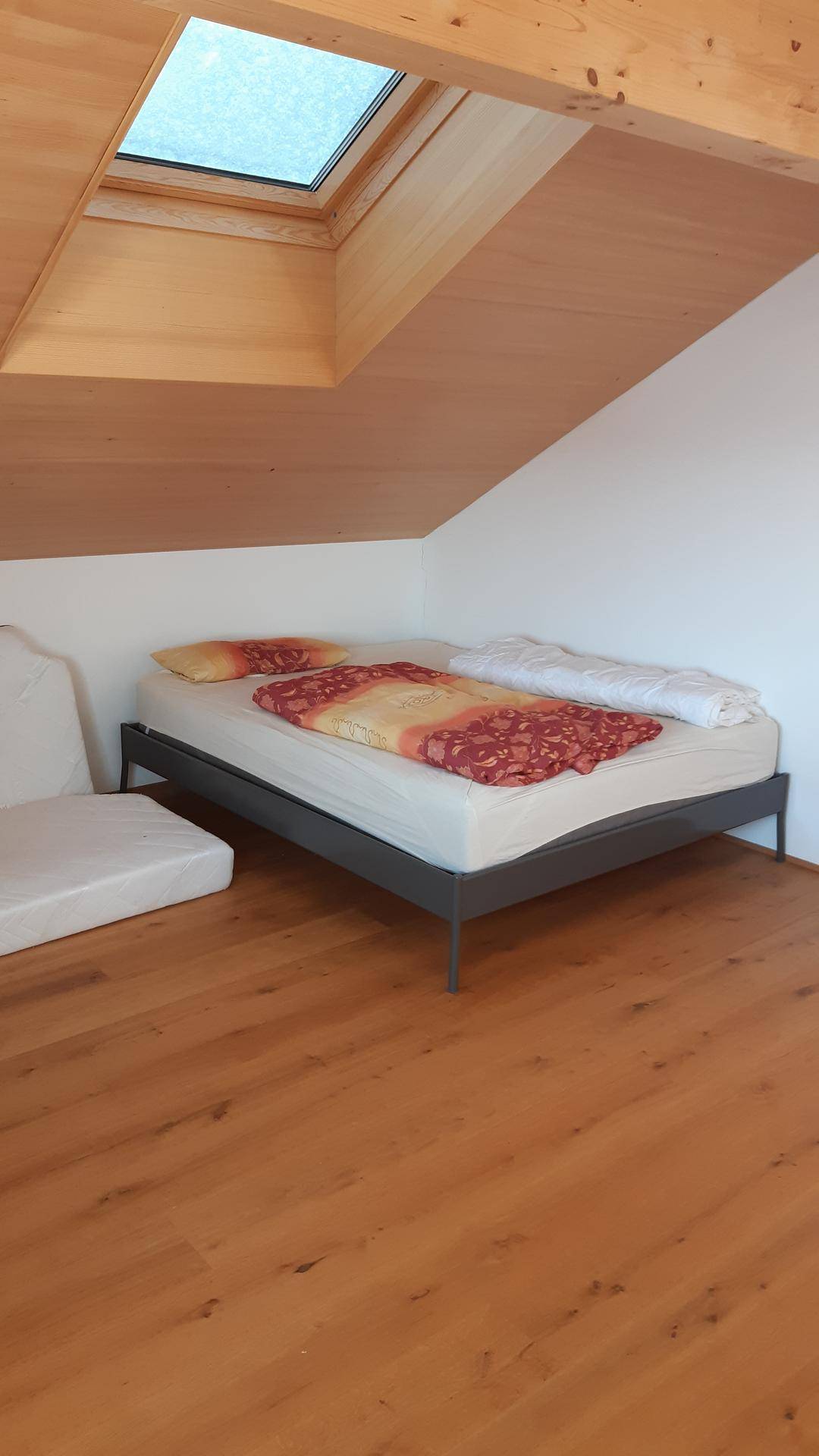 Gemütliches Schlafzimmer im Dachgeschoss mit Holzboden, Bett und einem Oberlicht für natürliches Licht.