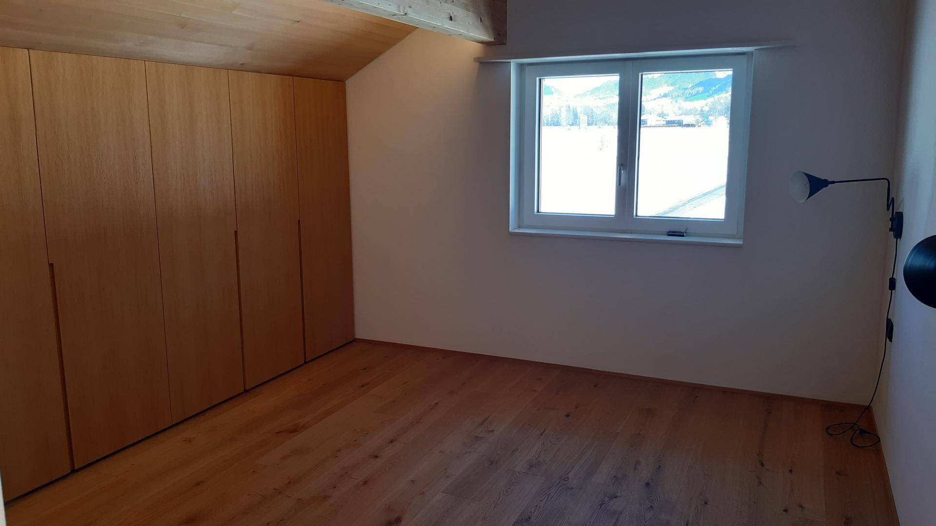 Schlafzimmer mit Einbauschränken, Holzboden und Fenster mit Blick auf die verschneite Landschaft.