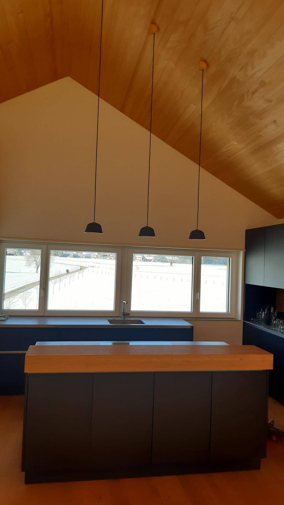 Moderne Küche mit dunklen Schränken, Holz-Arbeitsplatte auf der Insel und großen Fenstern.