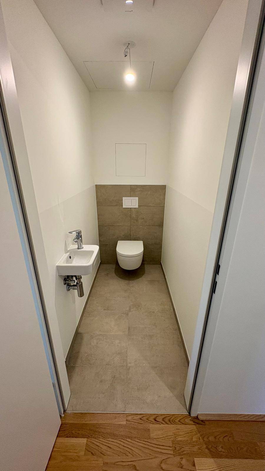 Kompaktes Gäste-WC mit Wand-WC, kleinem Waschbecken und modernen Fliesen an der Wand.