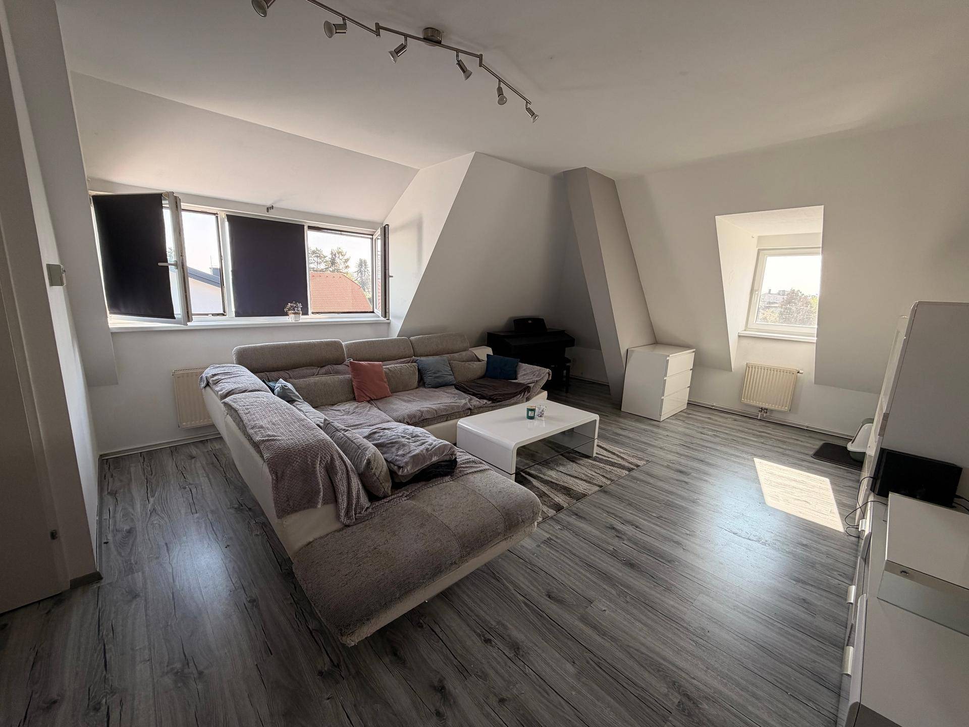Geräumiges Wohnzimmer im Dachgeschoss mit großem Sofa, Couchtisch und mehreren Fenstern für Helligkeit.