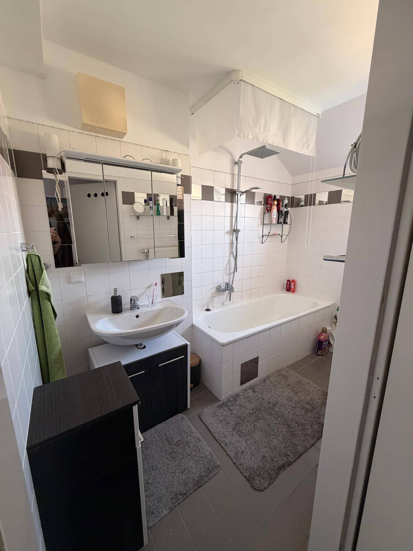 Badezimmer mit Badewanne, Duschfunktion, Waschbecken und Spiegelschrank, in hellen Fliesen gehalten.