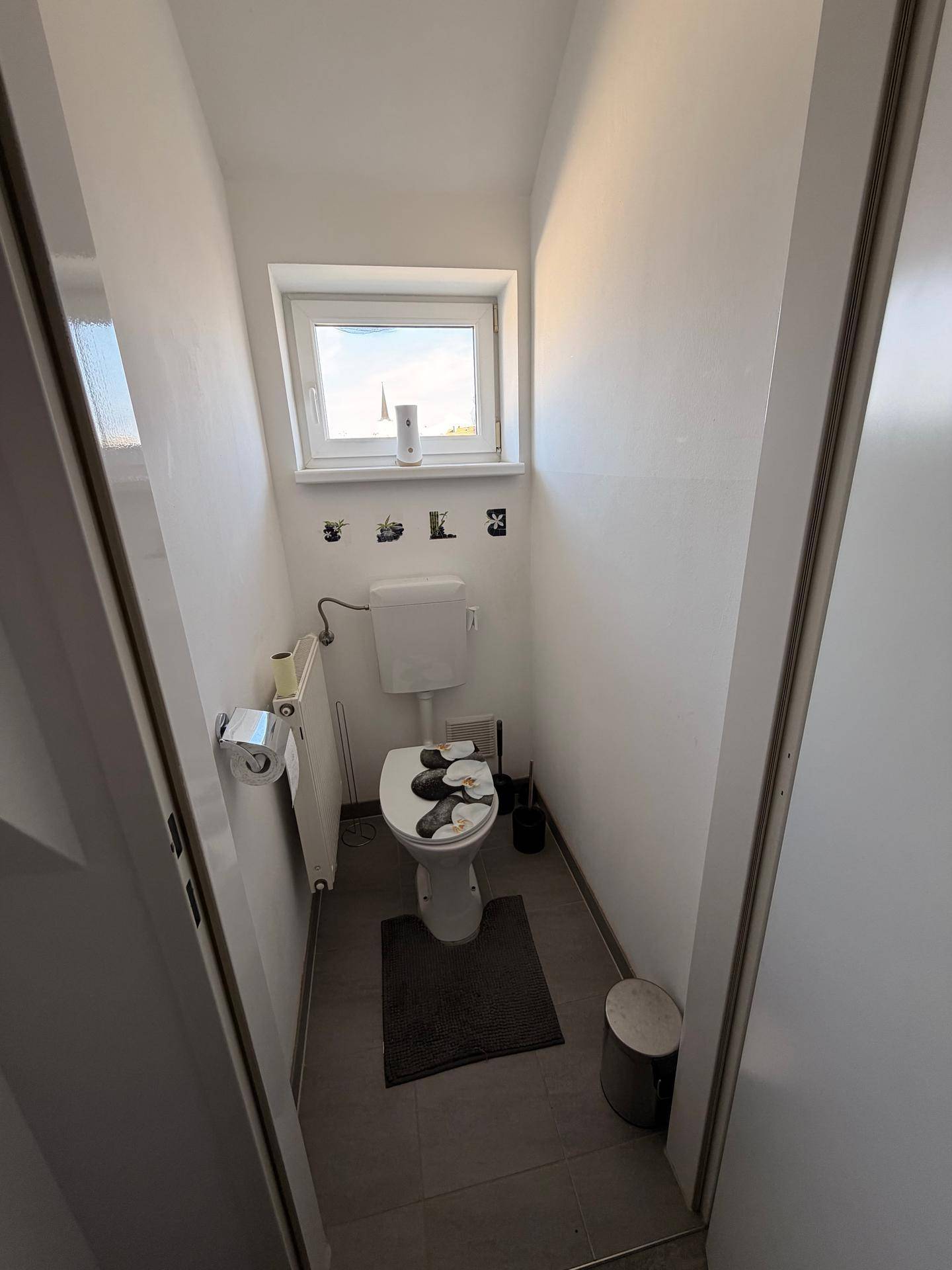 Separates WC mit Fenster für natürliche Belüftung und Tageslicht, in schlichtem Design und hellen Fliesen.