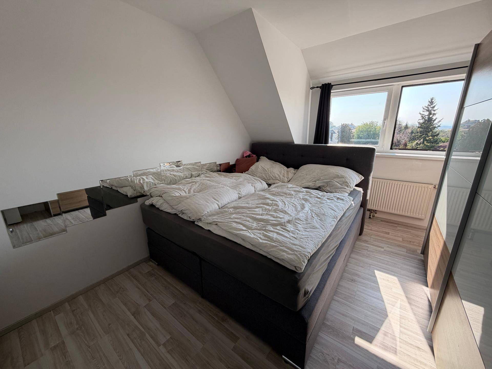 Gemütliches Schlafzimmer im Dachgeschoss mit Doppelbett und Fenster, das eine grüne Aussicht bietet.