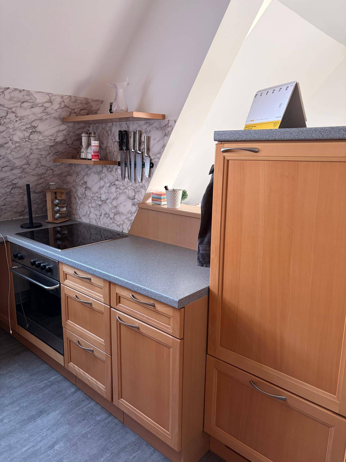 Funktionale Küche mit Kochfeld, Backofen und Holzschränken, ergänzt durch eine moderne Rückwand in Marmoroptik.